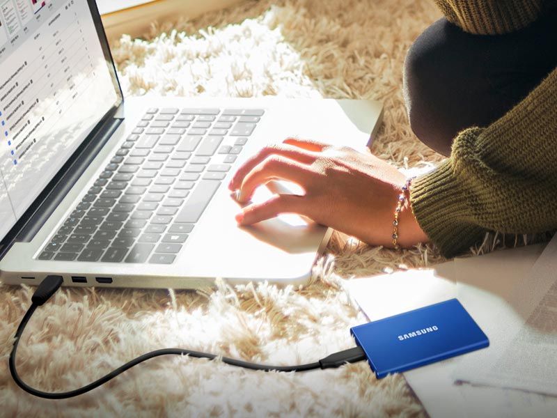 blue samsung portable ssd on rug with laptop that person is using