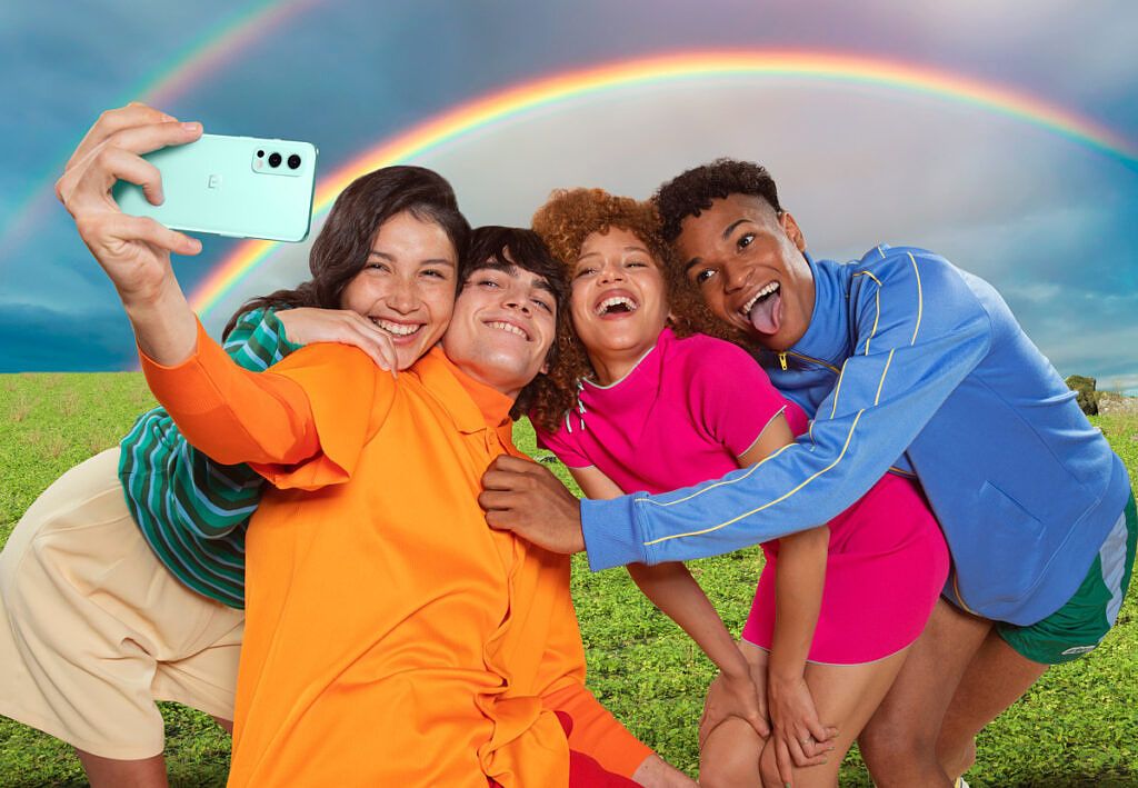 People posing with a rainbow in the background and clicking selfie photos with the OnePlus Nord 2 in hand