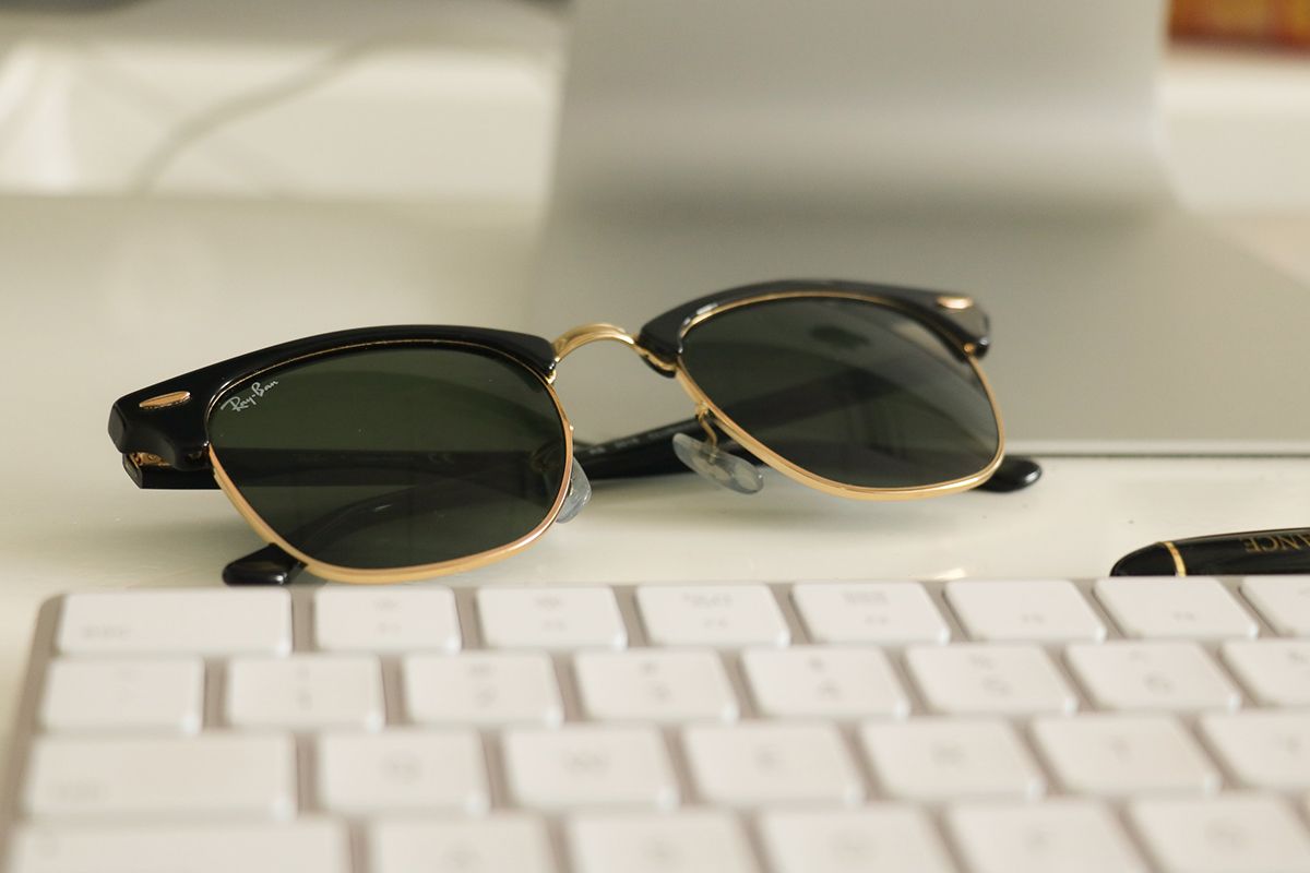 Ray-Ban sunglasses on white desk next to keyboard