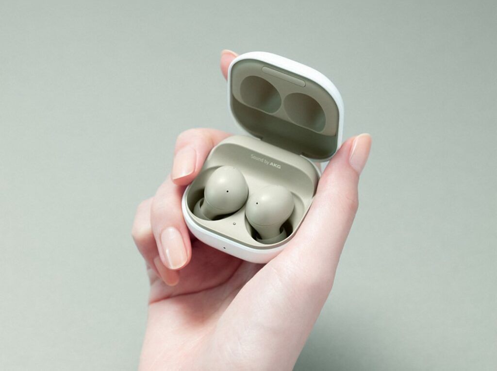 Samsung Galaxy Buds 2 in Olive Green side profile, held in hand, kept open in case, on an aqua green background