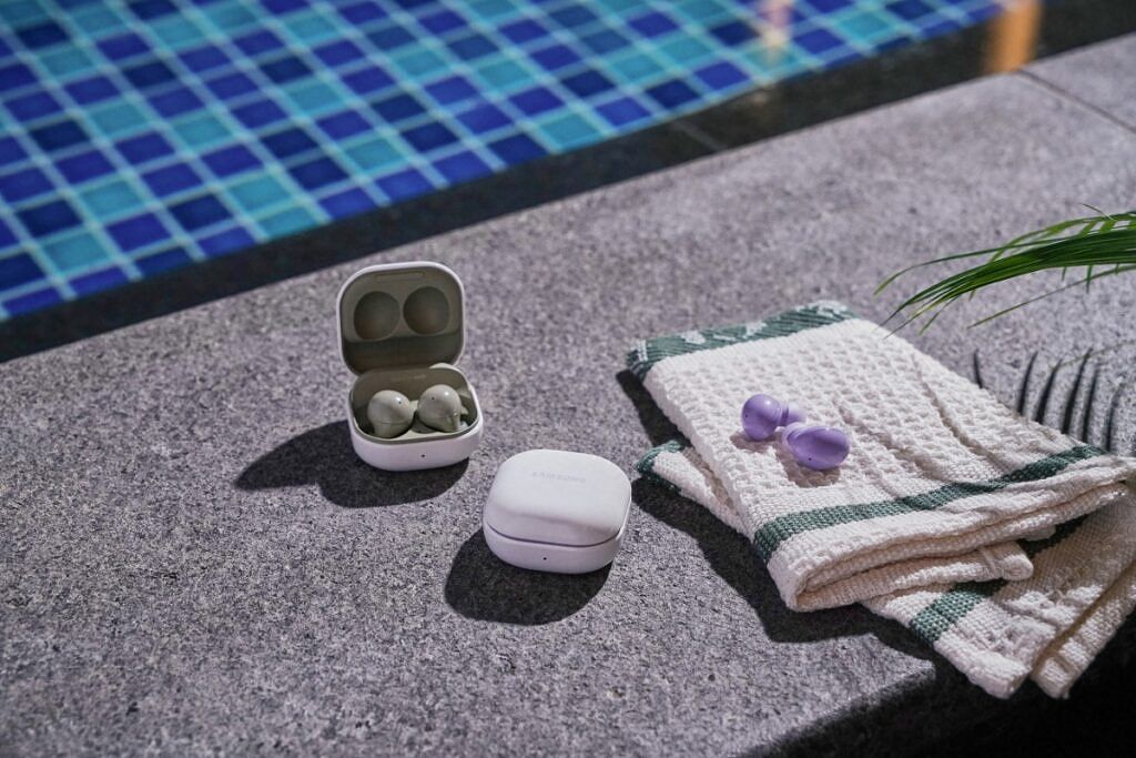 Samsung Galaxy Buds 2 in Olive Green and Lavender Purple kept besides a pool