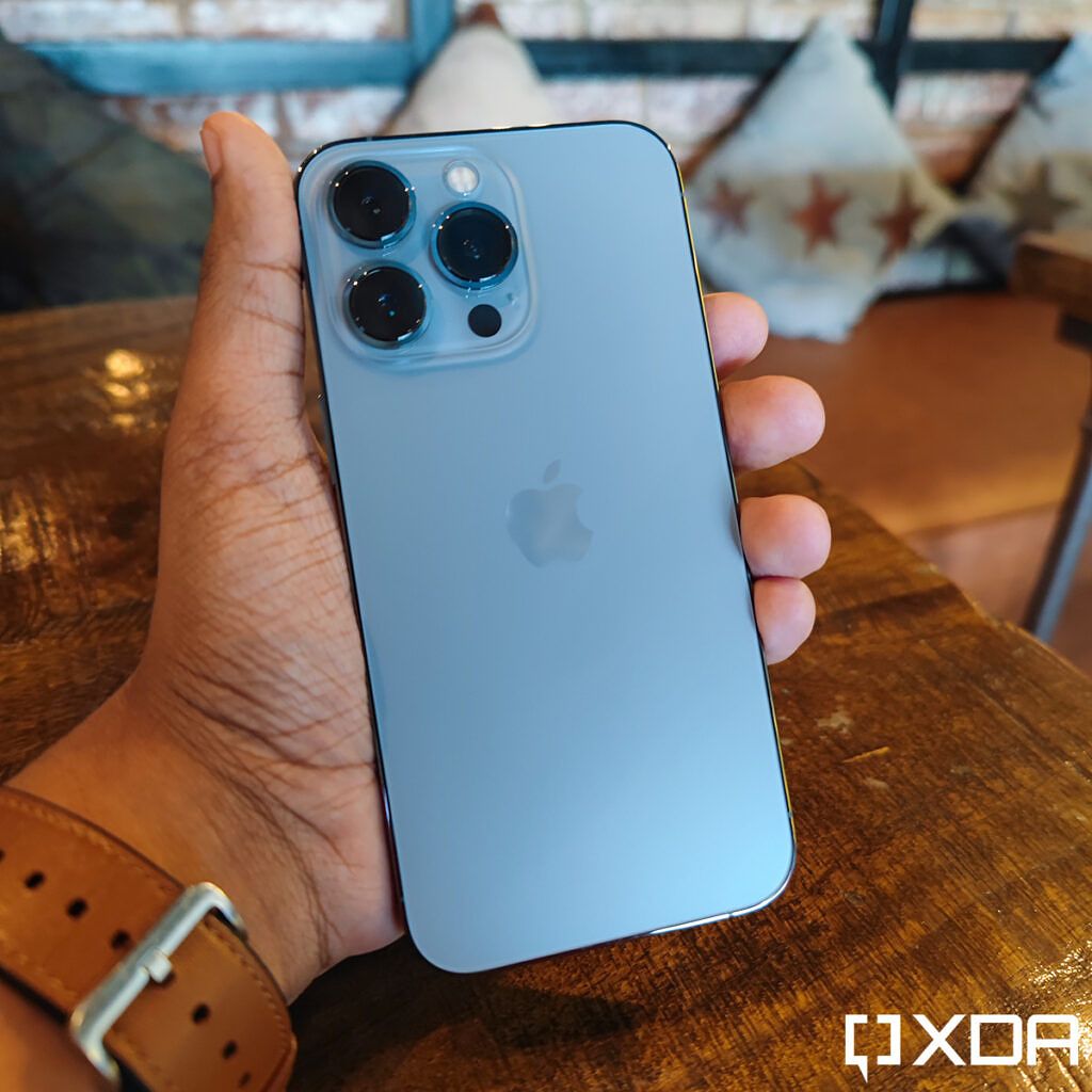 Apple iPhone 13 Pro Sierra Blue held out in hand, over a wooden table
