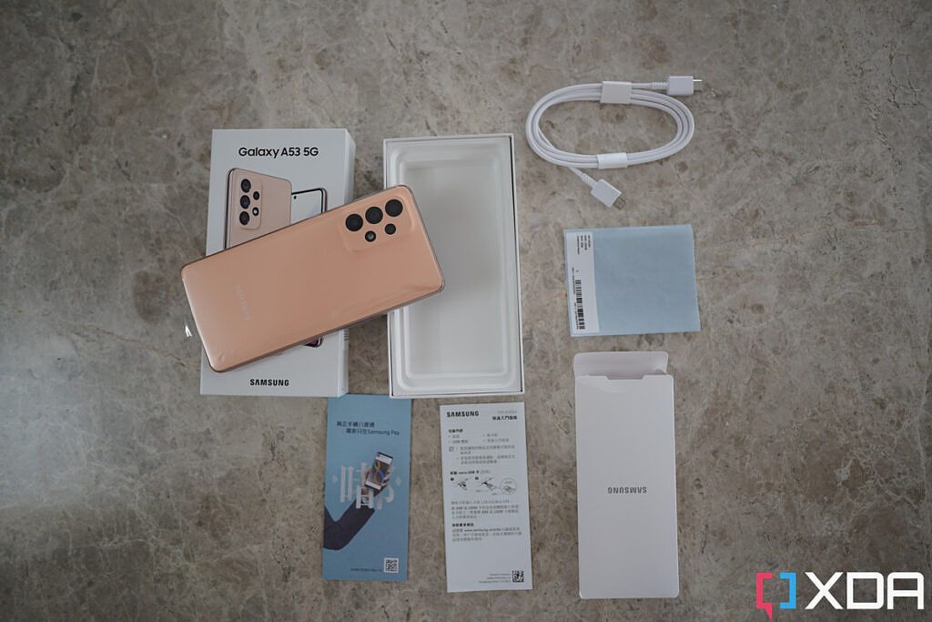 Box contents of the Samsung Galaxy A53 5G smartphone laid out: Includes the phone, a USB Type C to Type C cable, a SIM ejector tool, and region-specific documentation like Quick Start guides and more.