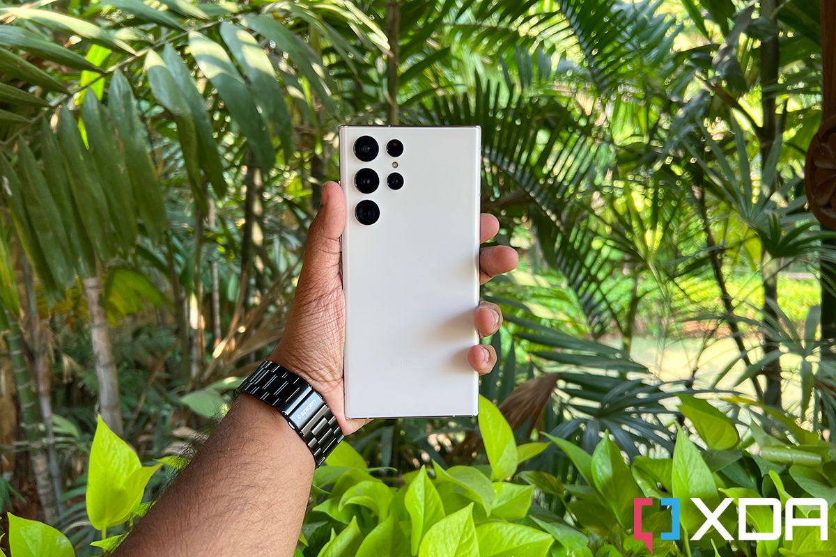 Samsung Galaxy S22 Ultra in Phantom White color held in hand against a foliage of green leaves in a garden