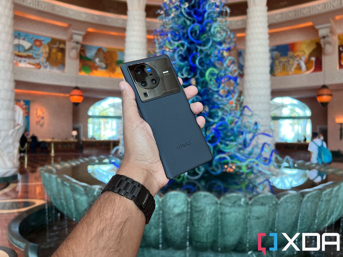 The Vivo X80 Pro held out in hand, in front of a fountain in a hotel lobby