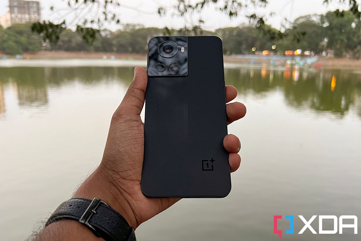 OnePlus 10R smartphone held out in hand, hand stretched out over a lake as the backdrop