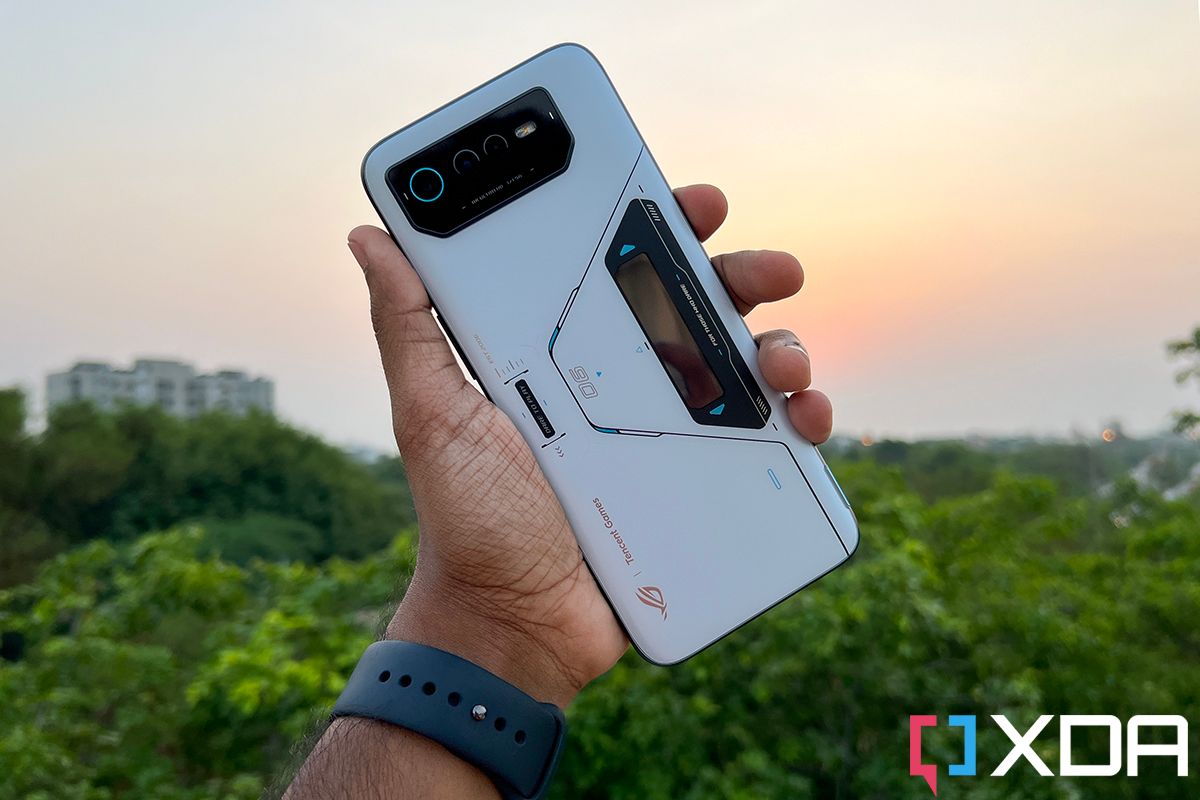 ASUS ROG Phone 6 Pro held out in the hand, against a canopy of trees with the sunset in the backdrop