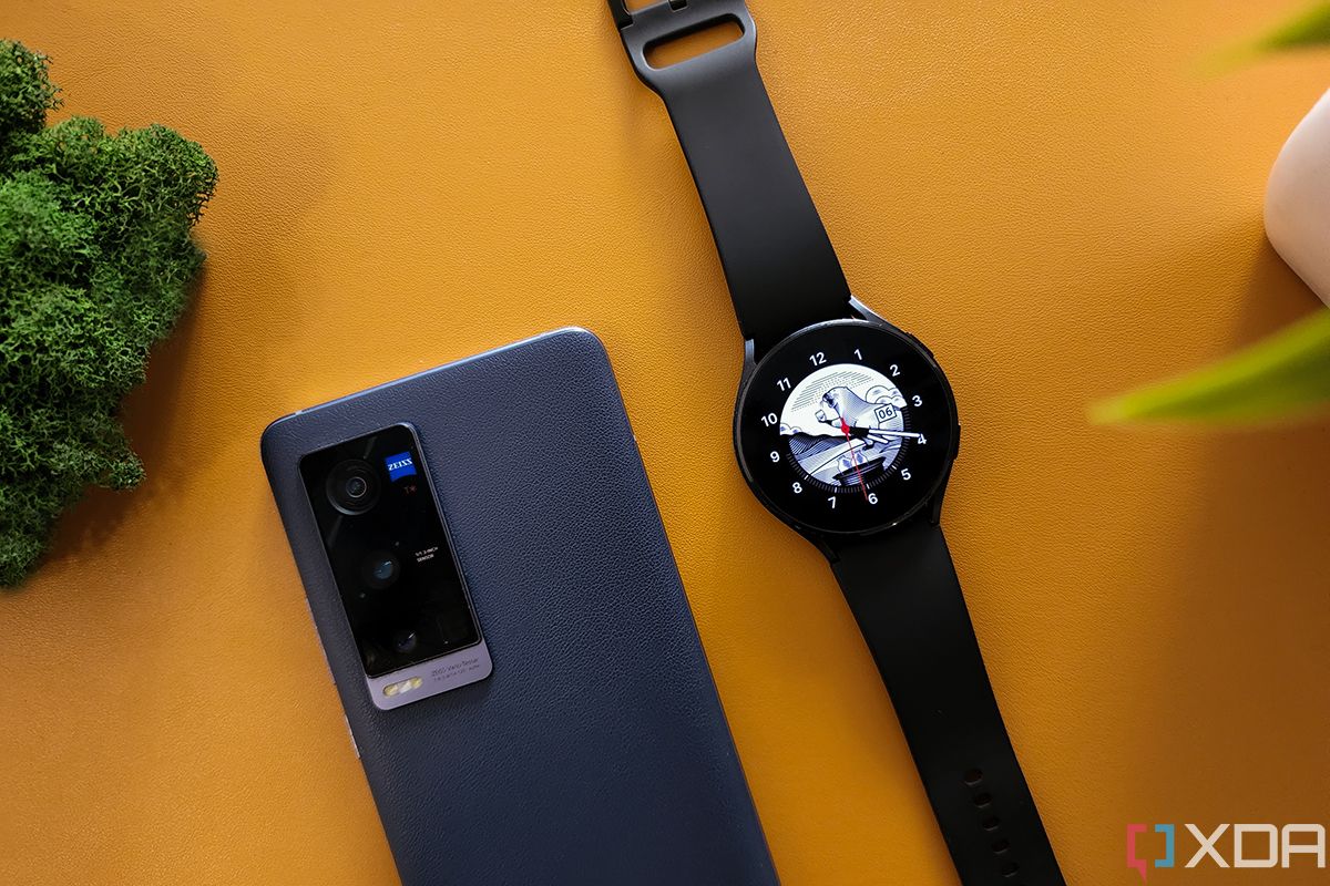 Galaxy Watch 4 next to Vivo smartphone on orange background.