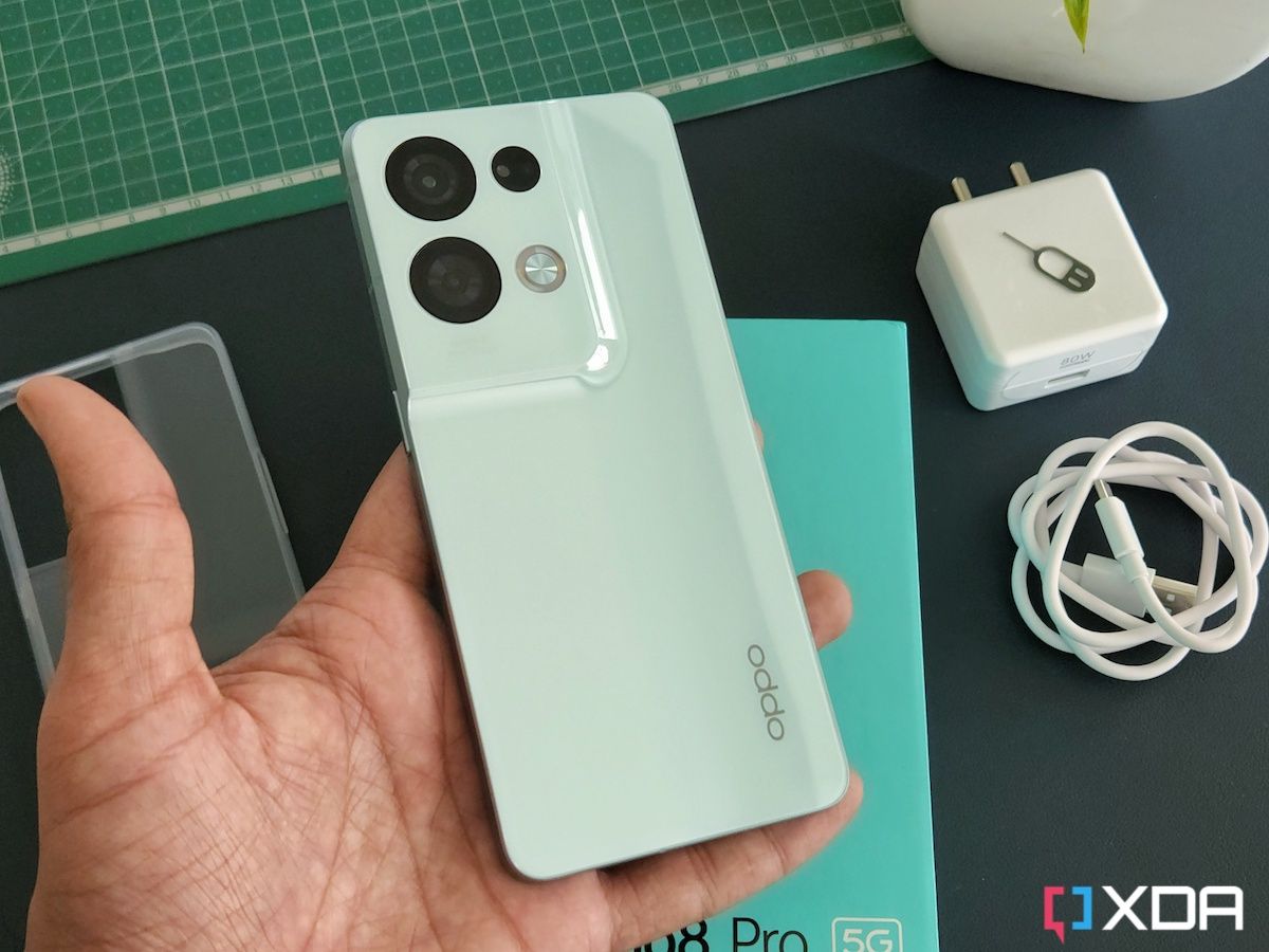 Oppo reno 8 Pro in hand with unboxed contents including a charger and USB cable in the background