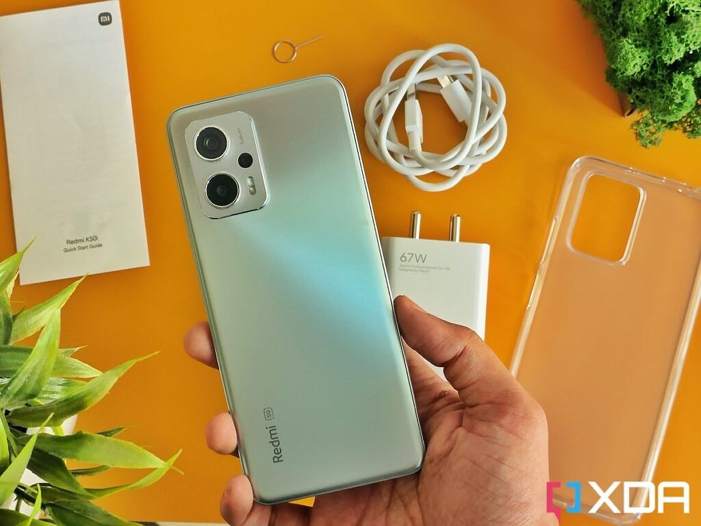 Redmi K50i smartphone on a yellow-color background next to its box contents