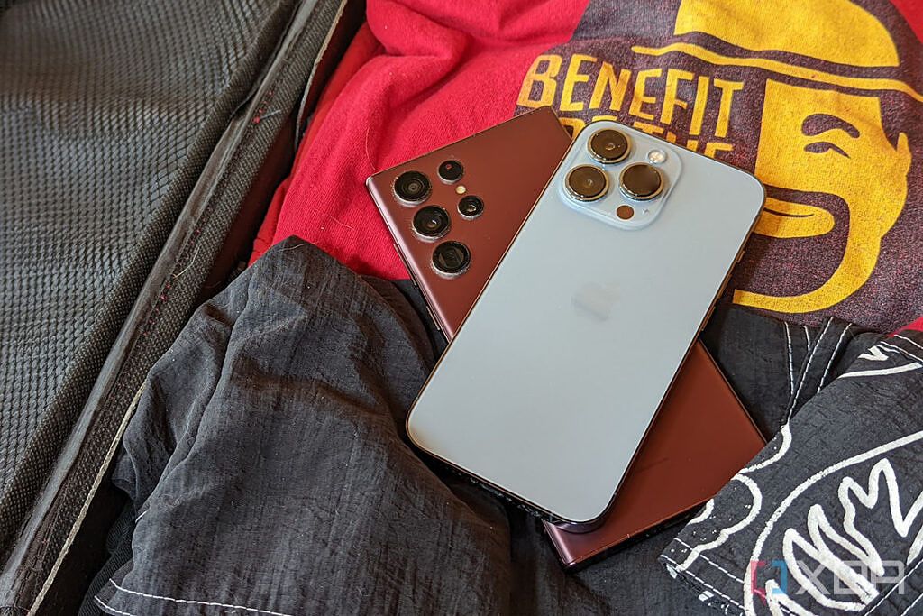 An iPhone 13 Pro and Samsung Galaxy S22 Ultra rest in a suitcase with clothes.