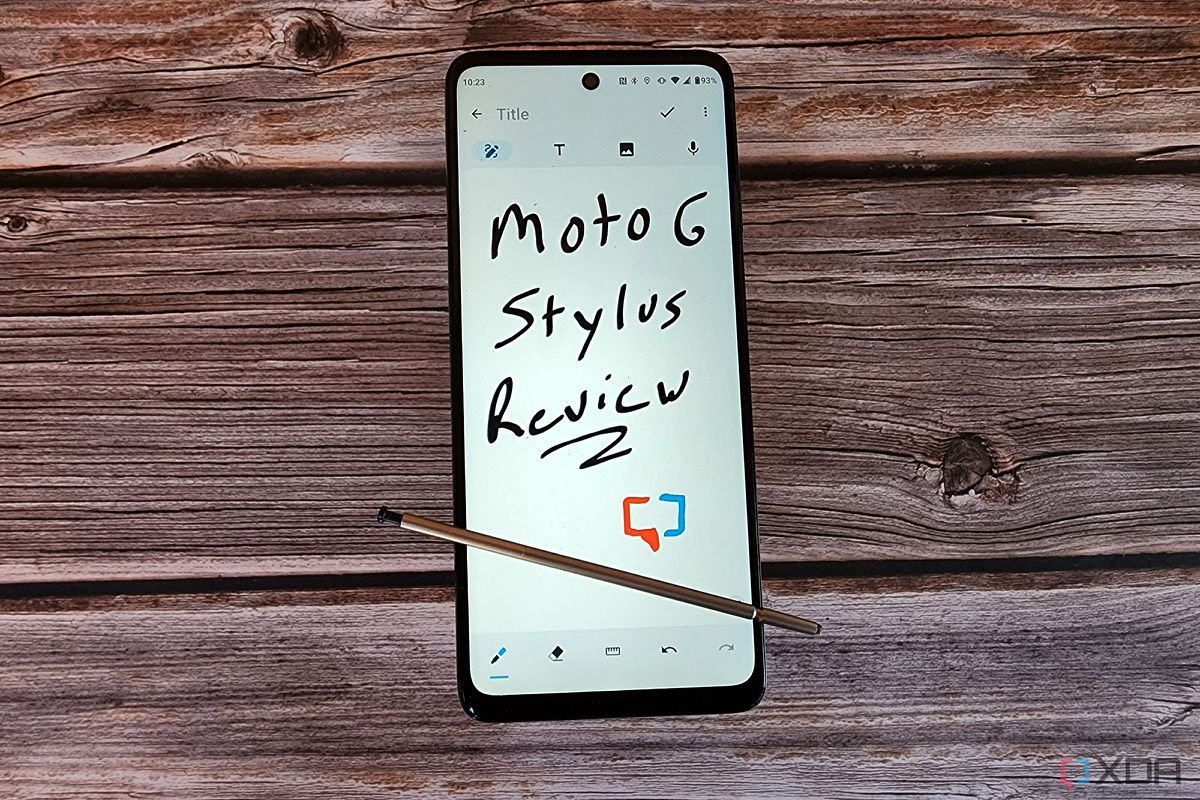 The Moto G stylus rests on a table with words written on the screen.