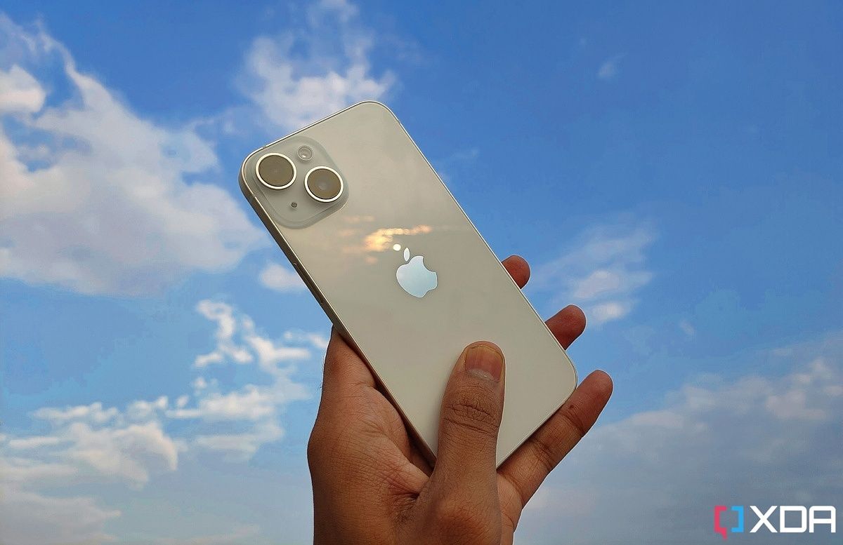 iPhone 14 in white holding hands against a blue sky background