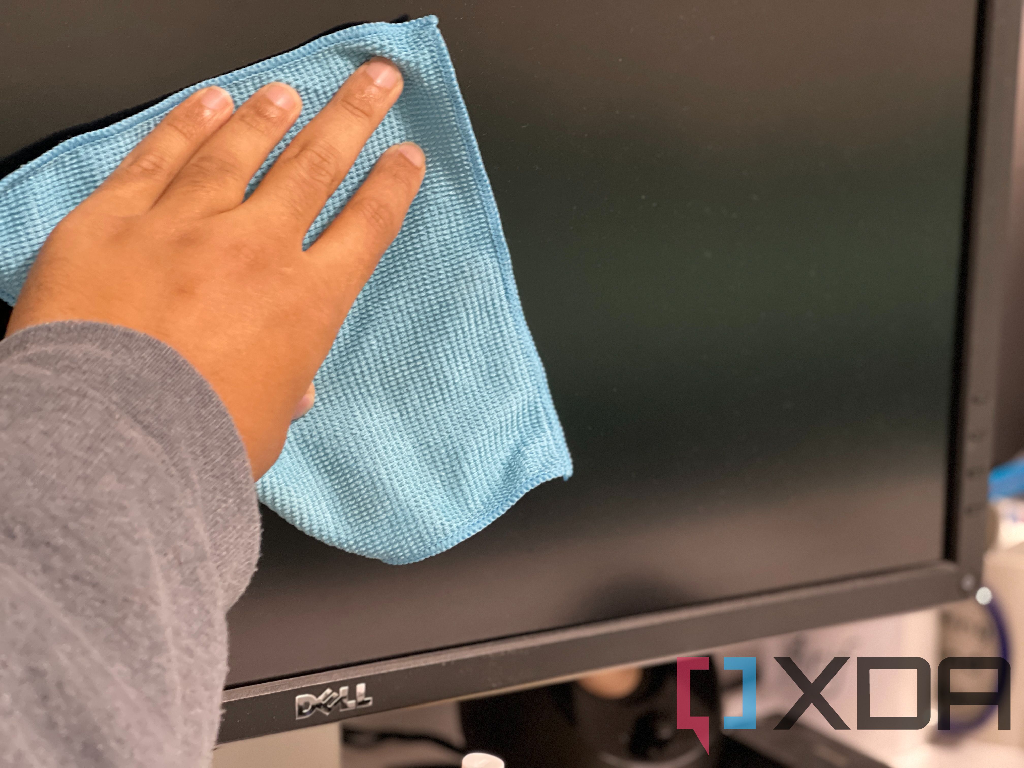 A person's hands holding a cloth over a monitor.