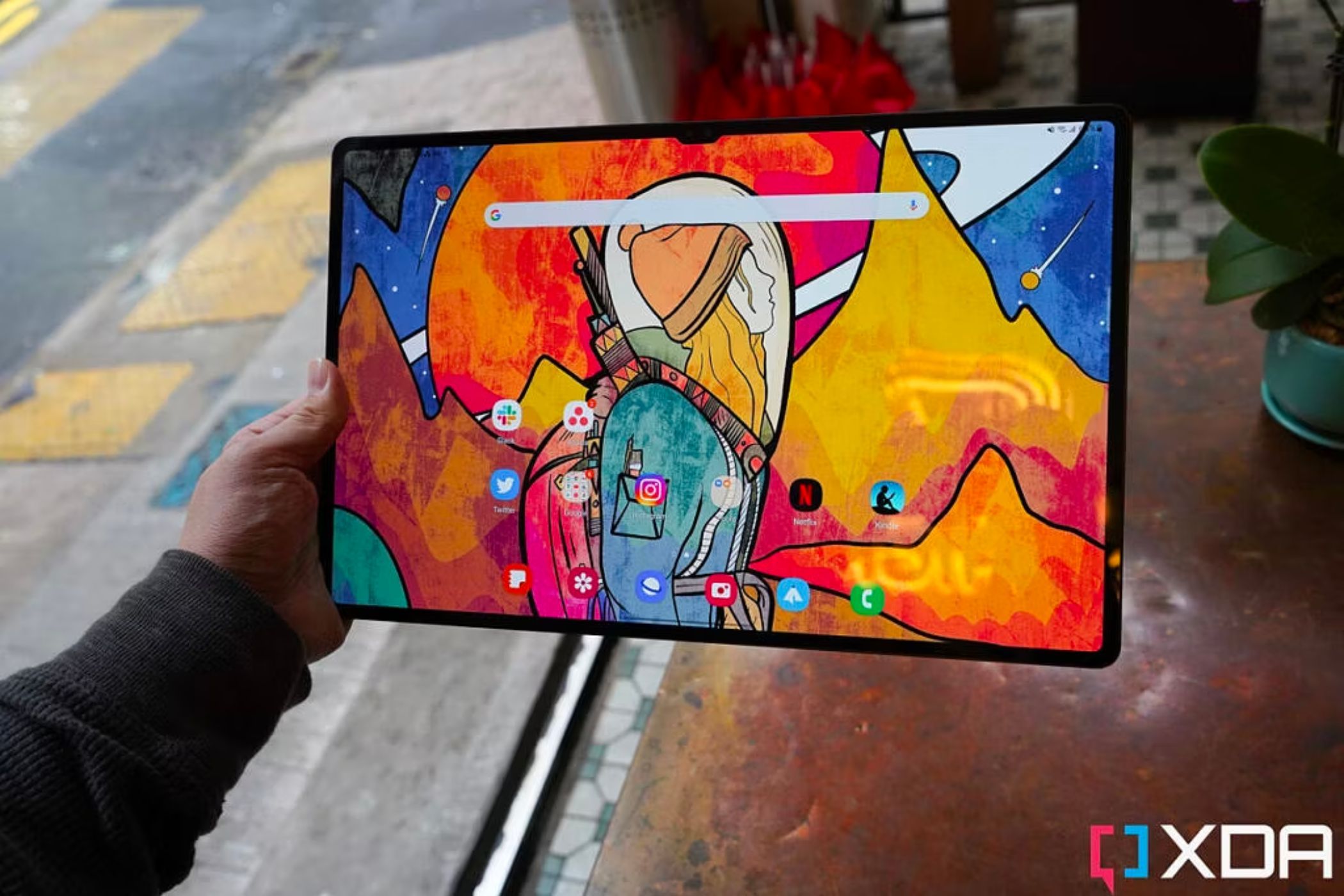 An image of a person holding a Samsung Galaxy Tab S8 Ultra tablet over a wooden table.