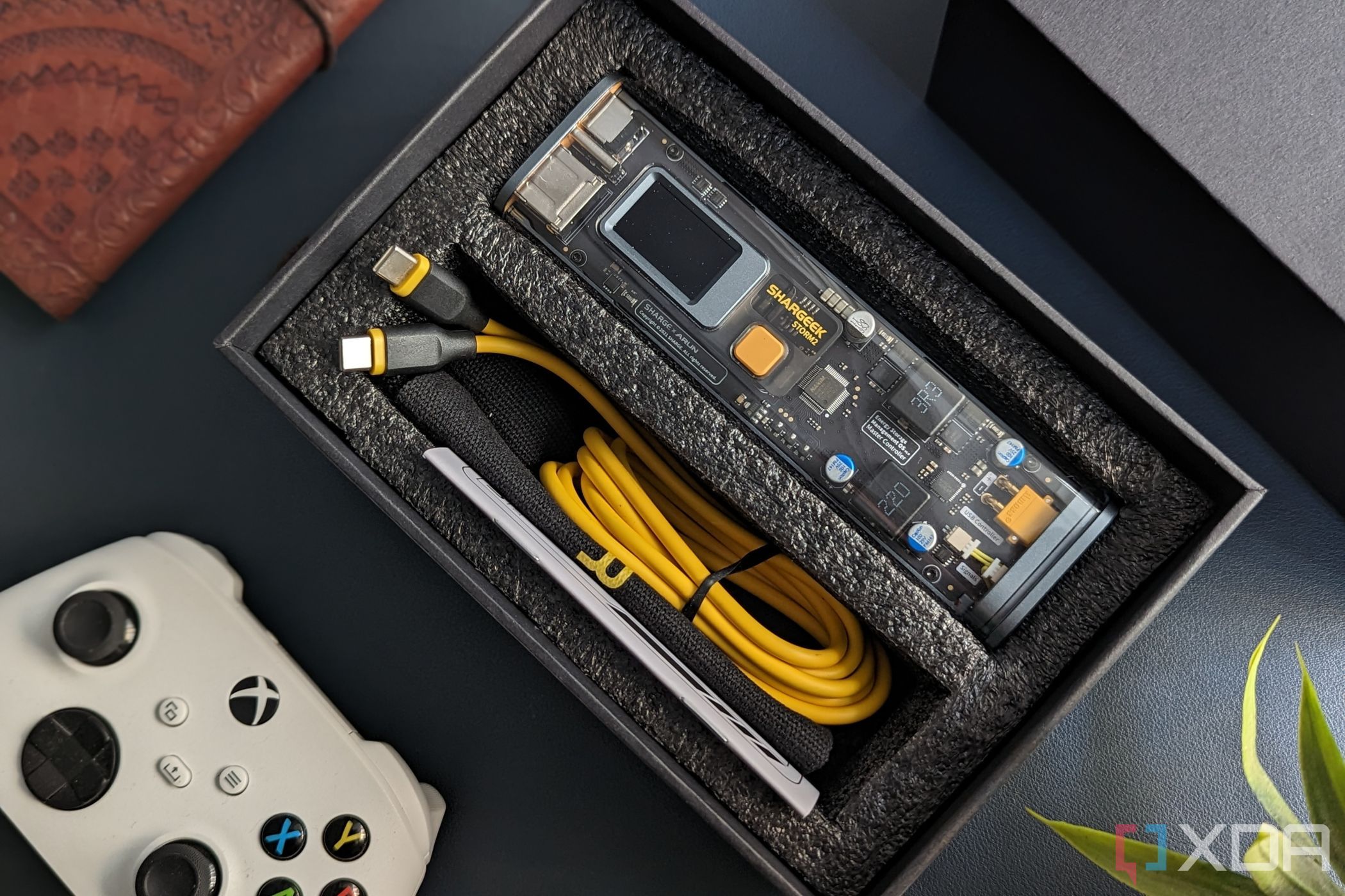 An image of the Chargeek Storm 2 battery pack in the box with its accessories that's kept on a leather desk mat with other miscellaneous items.
