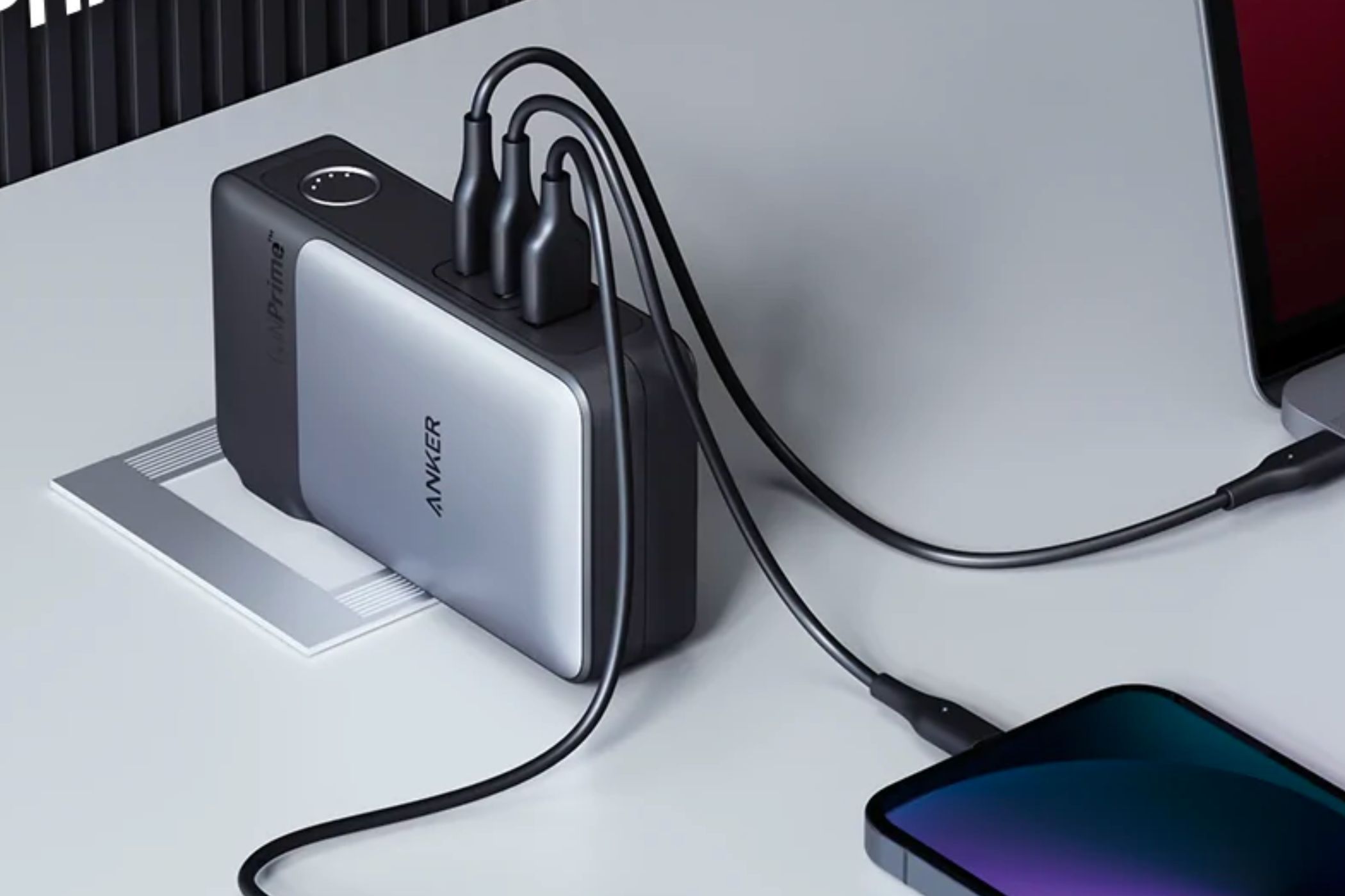 An image showing the Anker 733 power bank connected to an AC outlet on a white-colored table with multiple USB cables charging different devices.