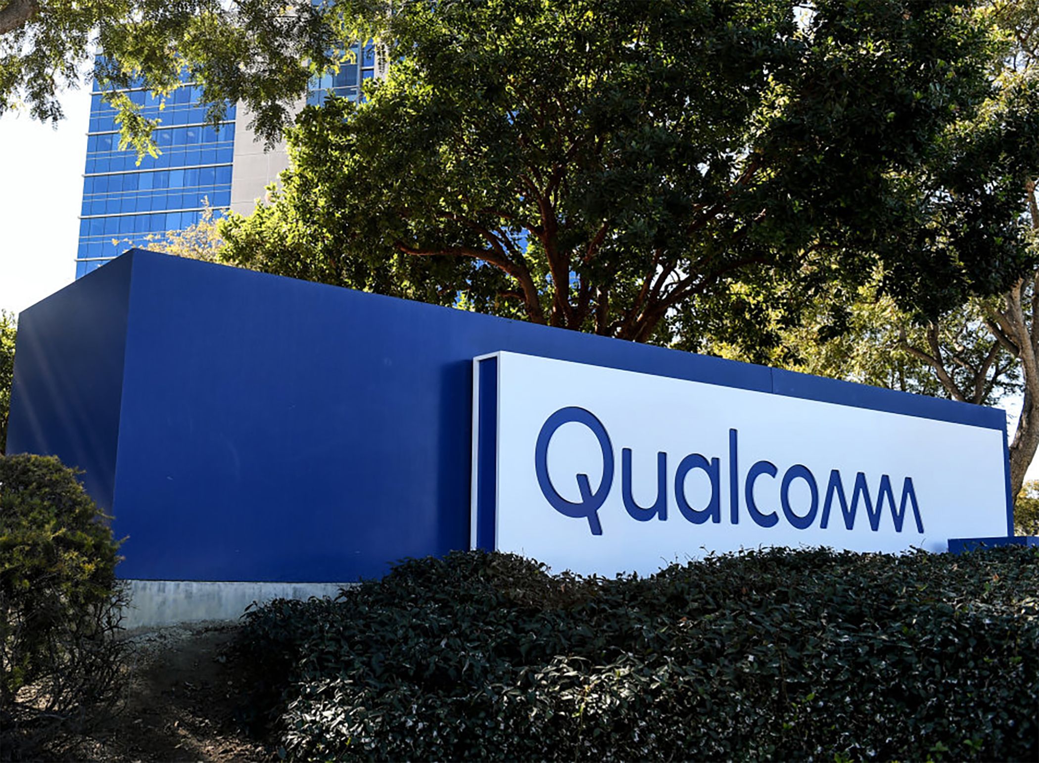 Qualcomm logo on sign surrounded by trees and plants.