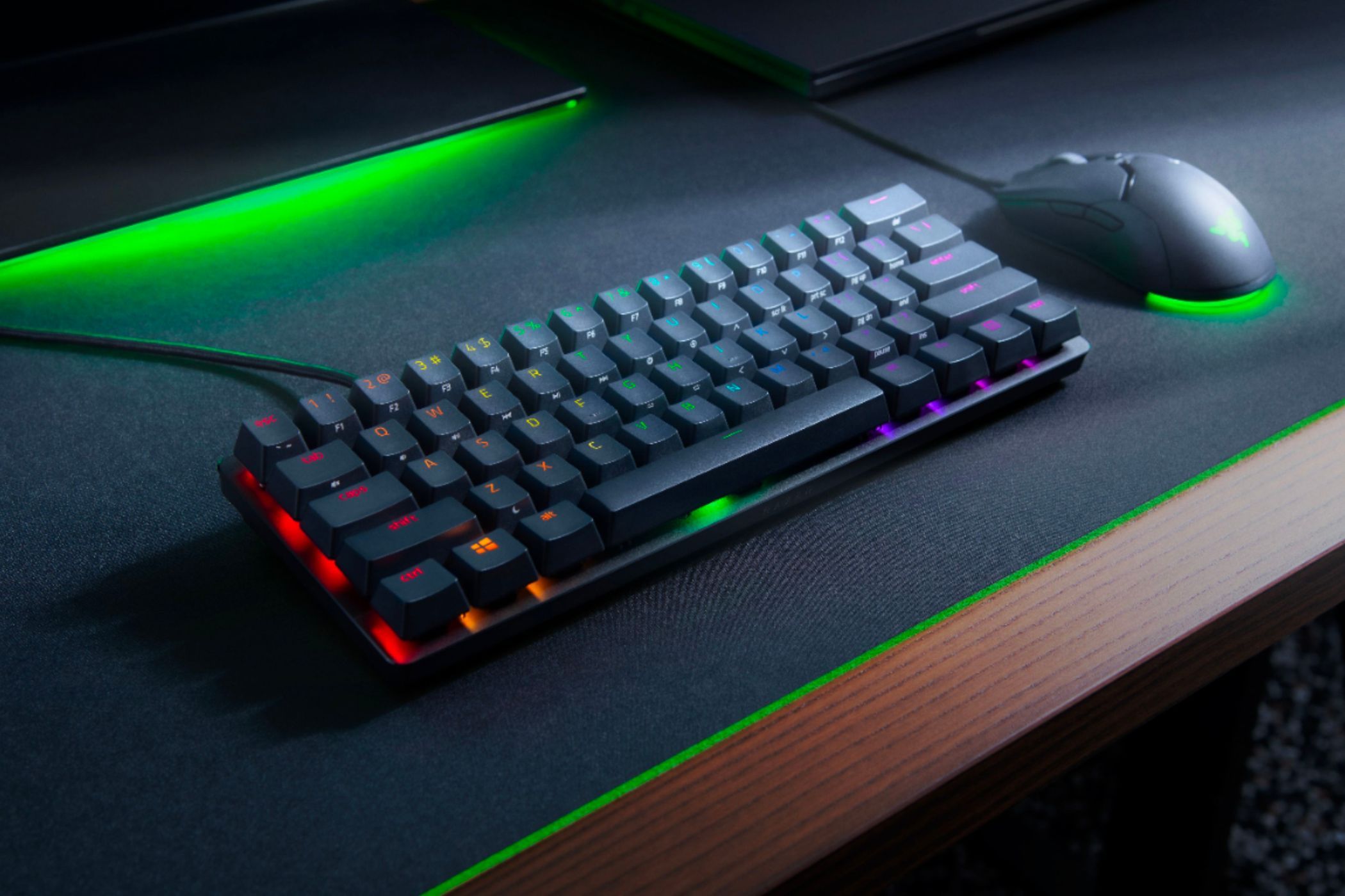 An image showing the Razer Huntsman mini keyboard next to a Razer mouse over a black-colored mousemat with green accents.