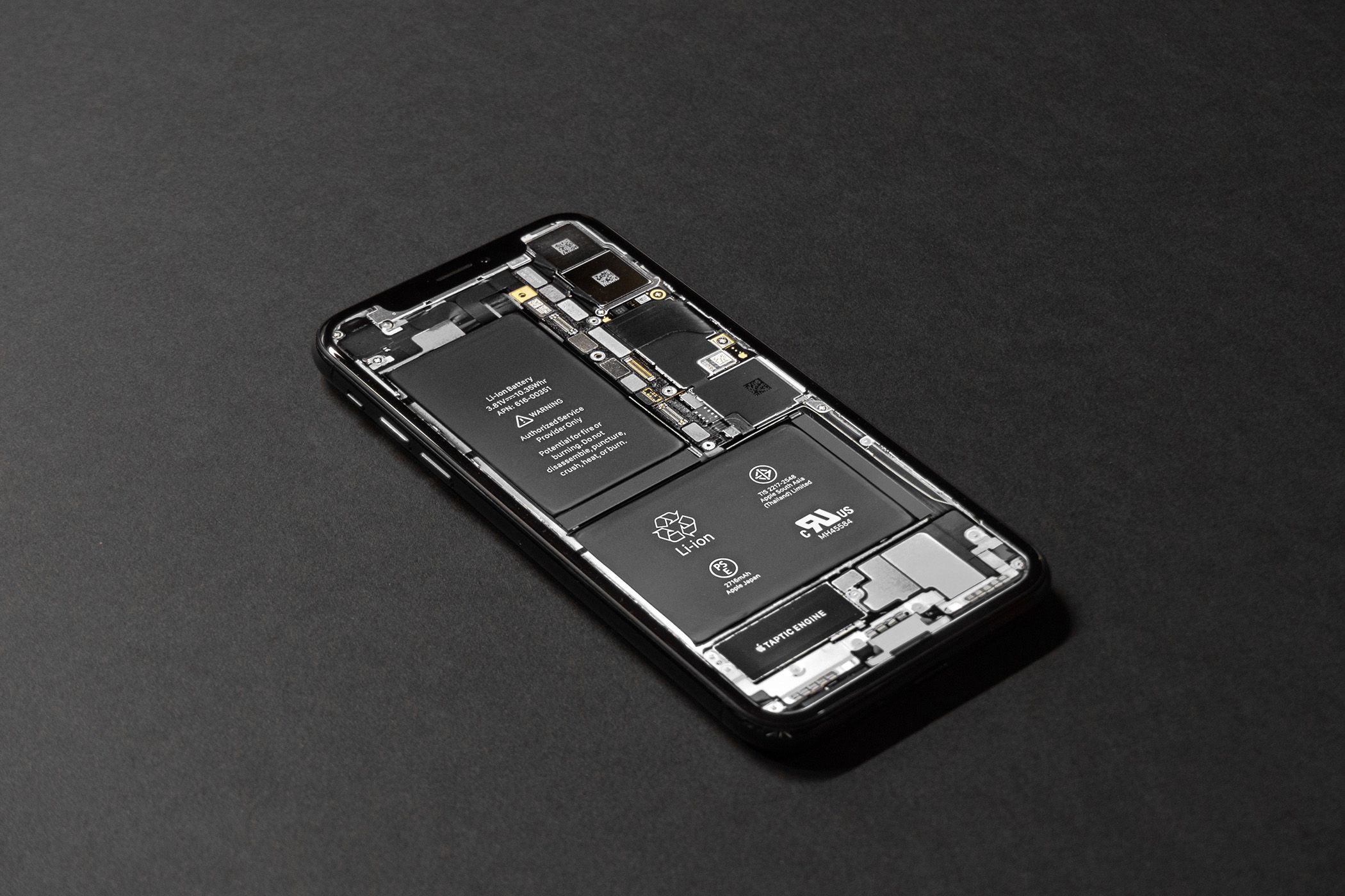 iPhone without screen showing the internal hardware on a black surface.