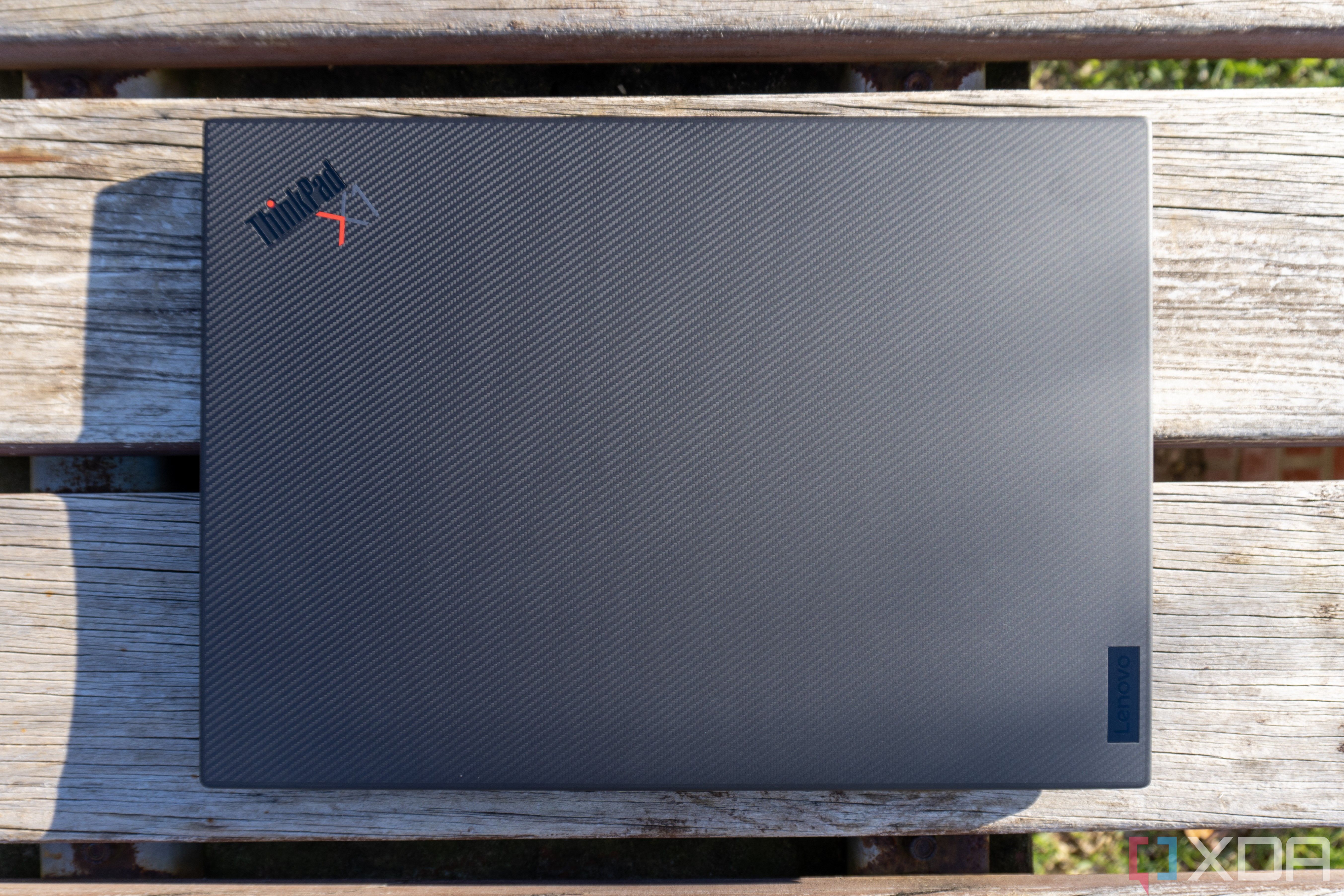 Overhead view of the Lenovo ThinkPad X1 Extreme Gen 5 laptop with the lid closed, showing the carbon fiber pattern on the lid, along with a Lenovo logo in the bottom right corner and a ThinkPad X1 logo in the top left