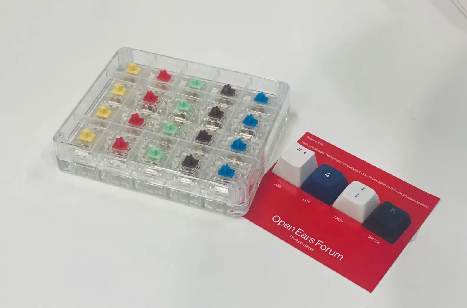 OnePlus Open Ears Forum card with various keycaps next to a mechanical keyboard switch tester pack.