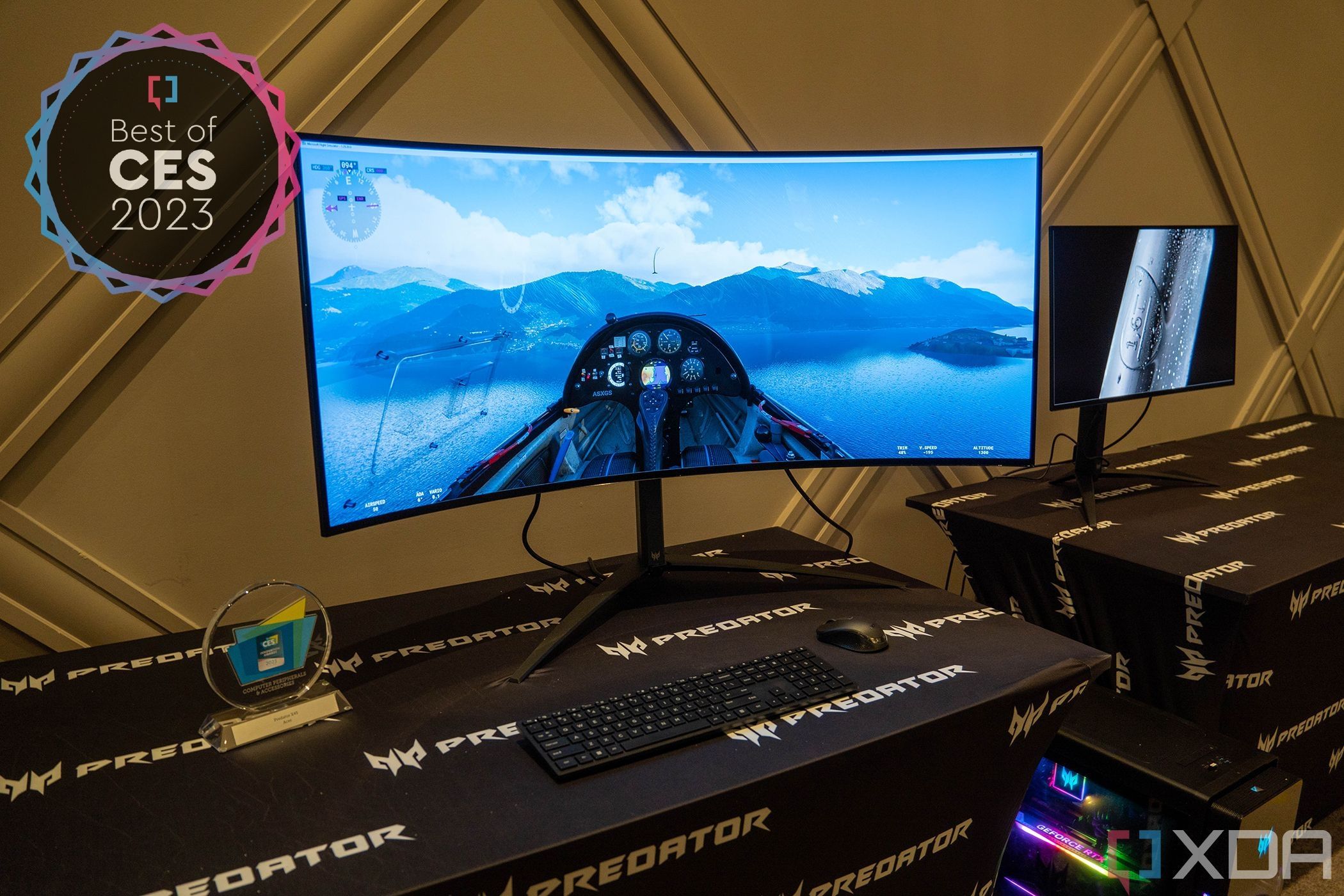 Front view of the Acer Predator X45 curved gaming monitor, displaying a first-person view inside the cockpit of an aircraft flying over water and with mountains in the distance. Overhead view of the Dell Premier Collaboration Keyboard with touch-based shortcuts for Zoom features. The top left corner of the image has a badge reading "Best of CES 2023"