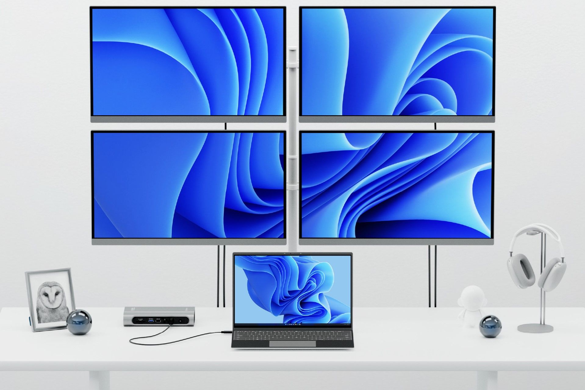 A laptop on a desk, connected to a docking station, which is connected to four displays on the wall behind the desk
