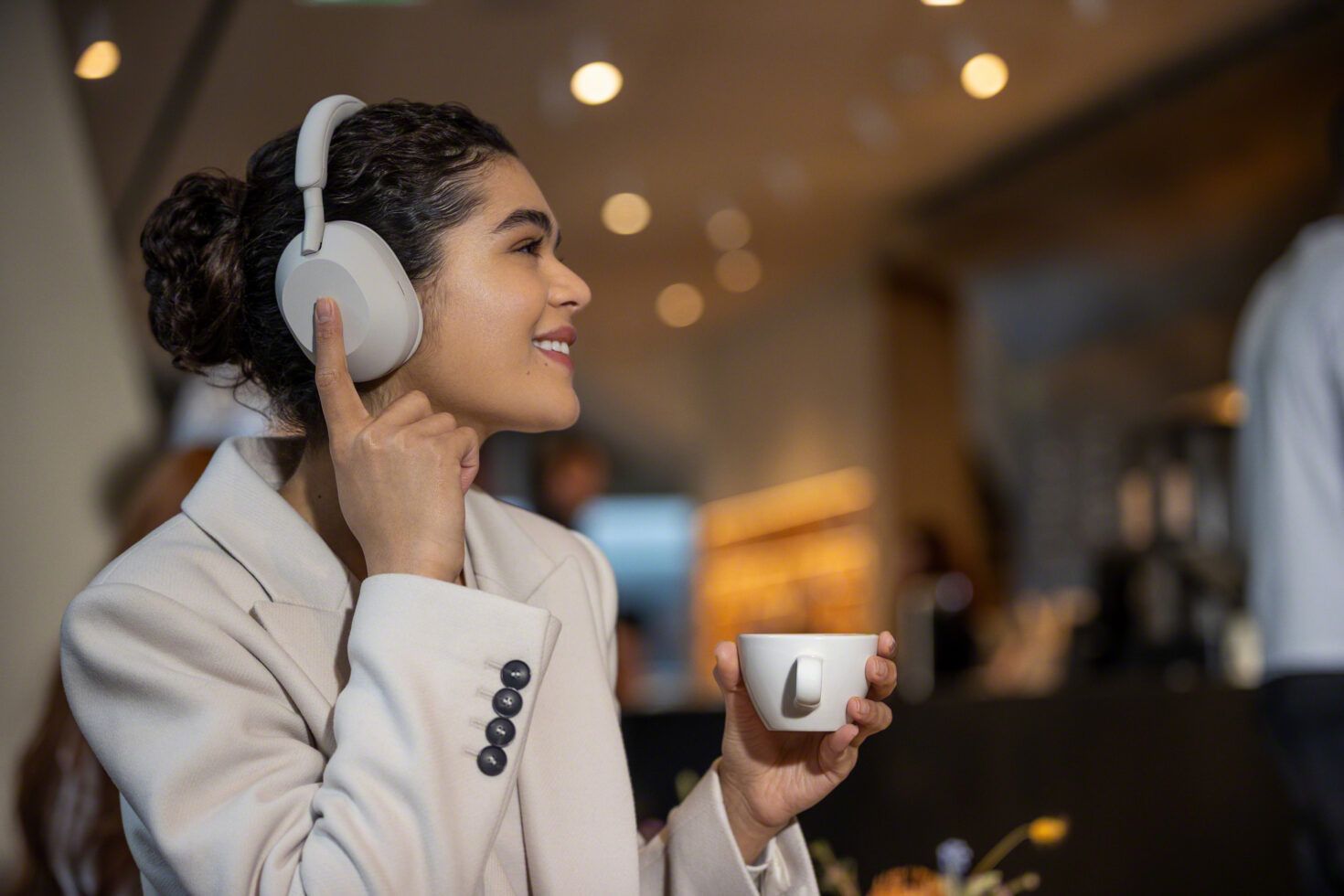 Woman wearing Sony WH-1000XM5 headphones with a cup of tea