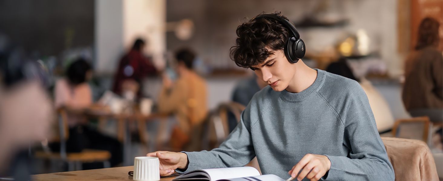 Una persona que usa auriculares Anker Soundcore Life Q30 mientras lee un libro y está sentada en una cafetería.