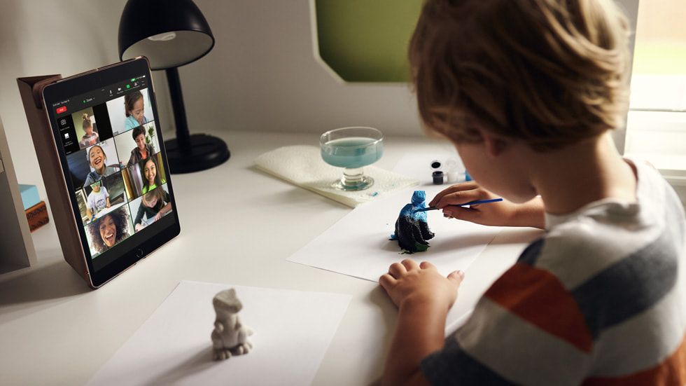 Un niño pintando figuras de arcilla en un escritorio mirando un iPad