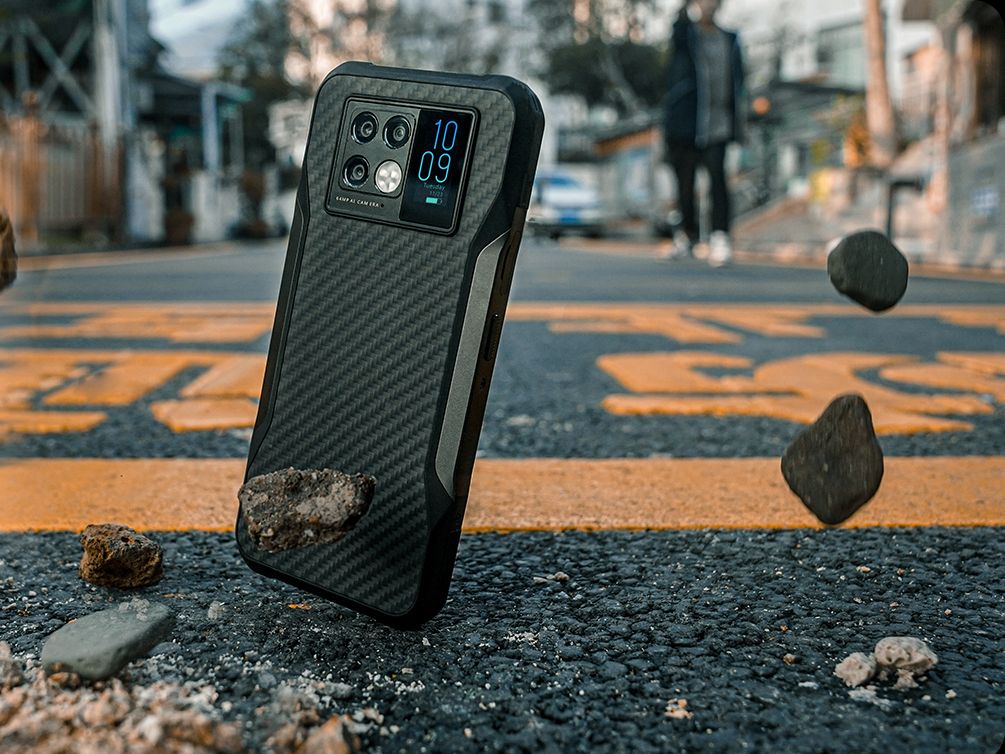 An image of a Doogee V20 phone falling onto pavement surrounded by some pebbles.