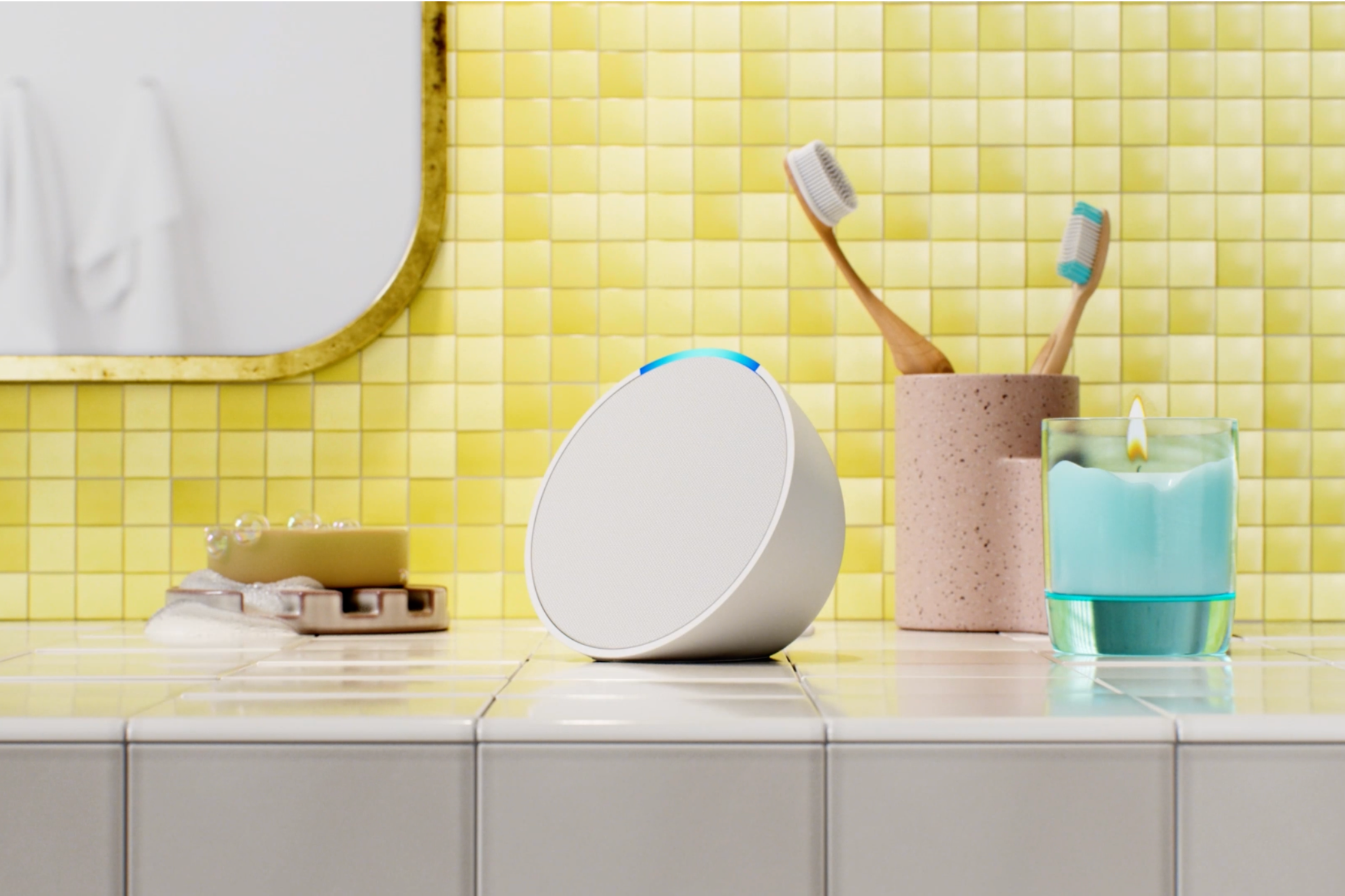 Amazon Echo Pop smart speaker in the bathroom with toothbrushes, sandle and soap in the background