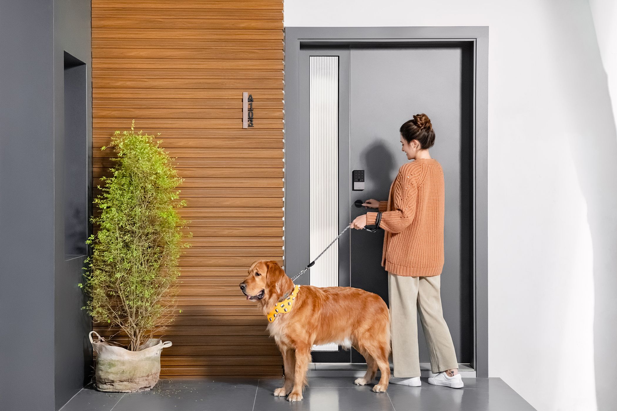 A woman opens her front door while holding her dog on a leash