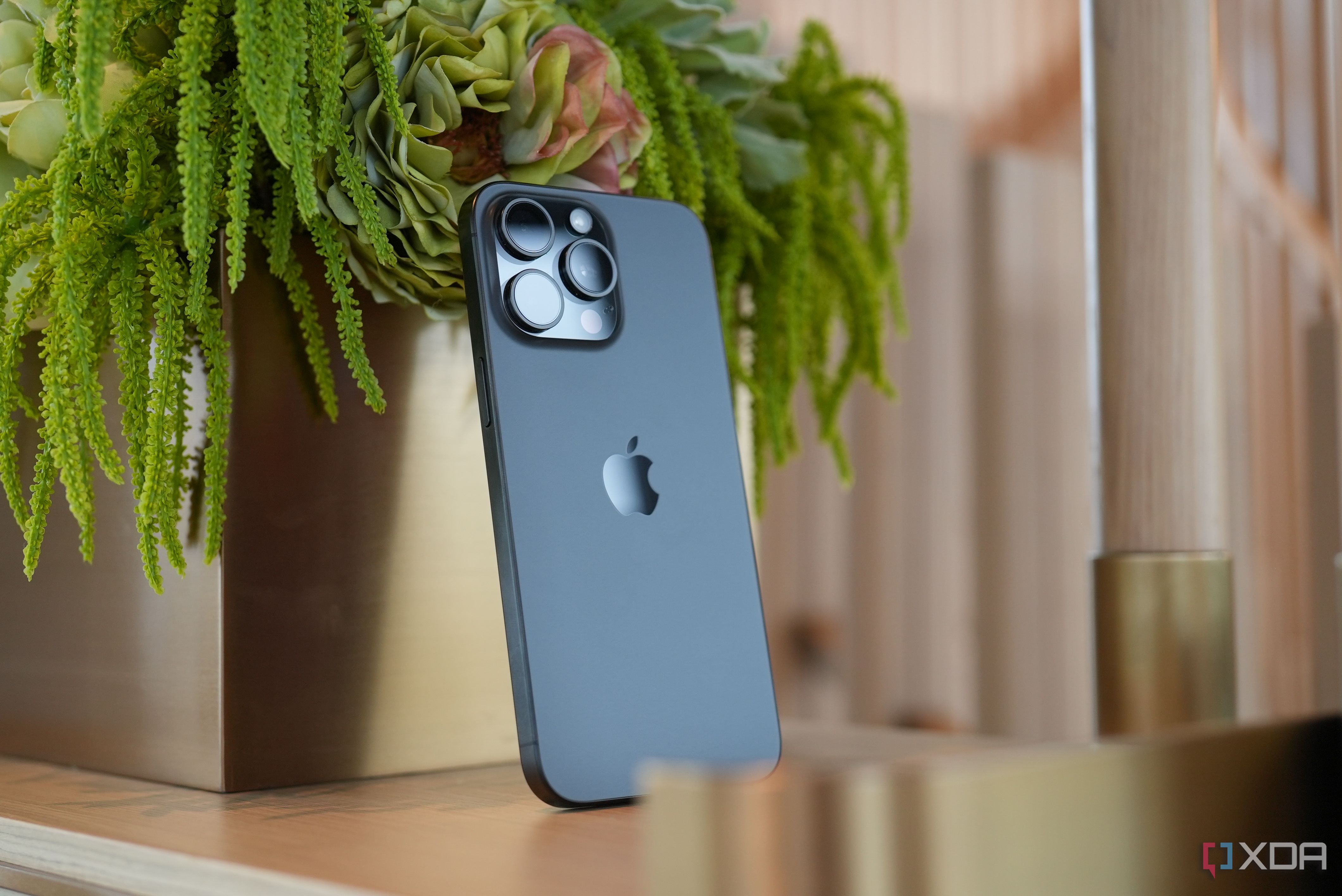 An iPhone 15 Pro Max propped up against a plant.