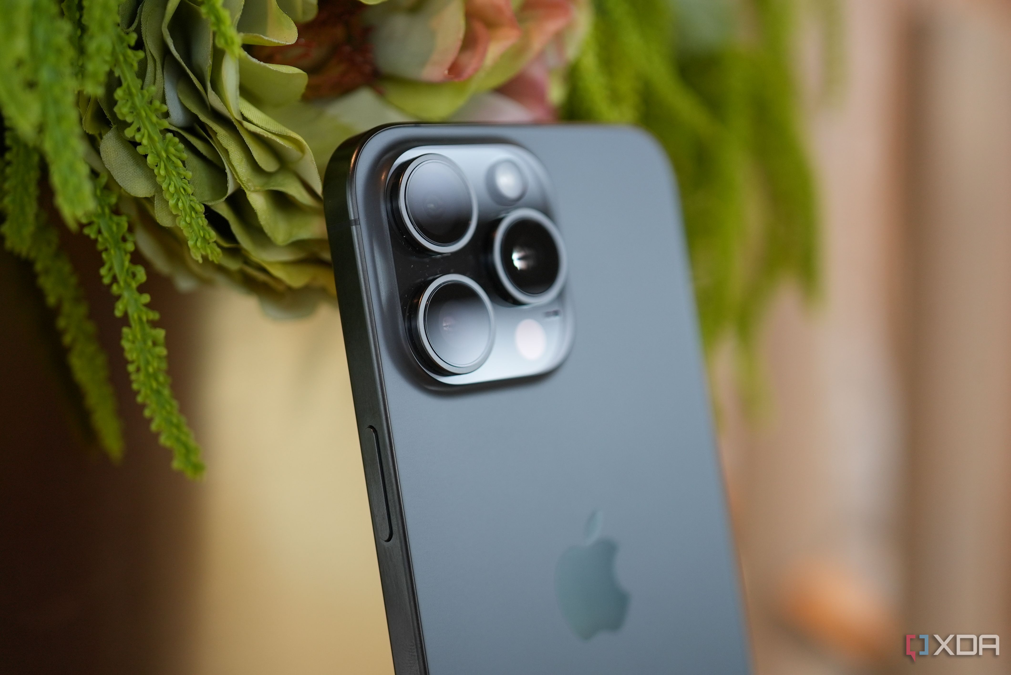iPhone 15 Pro Max in black titanium leaning against some plants