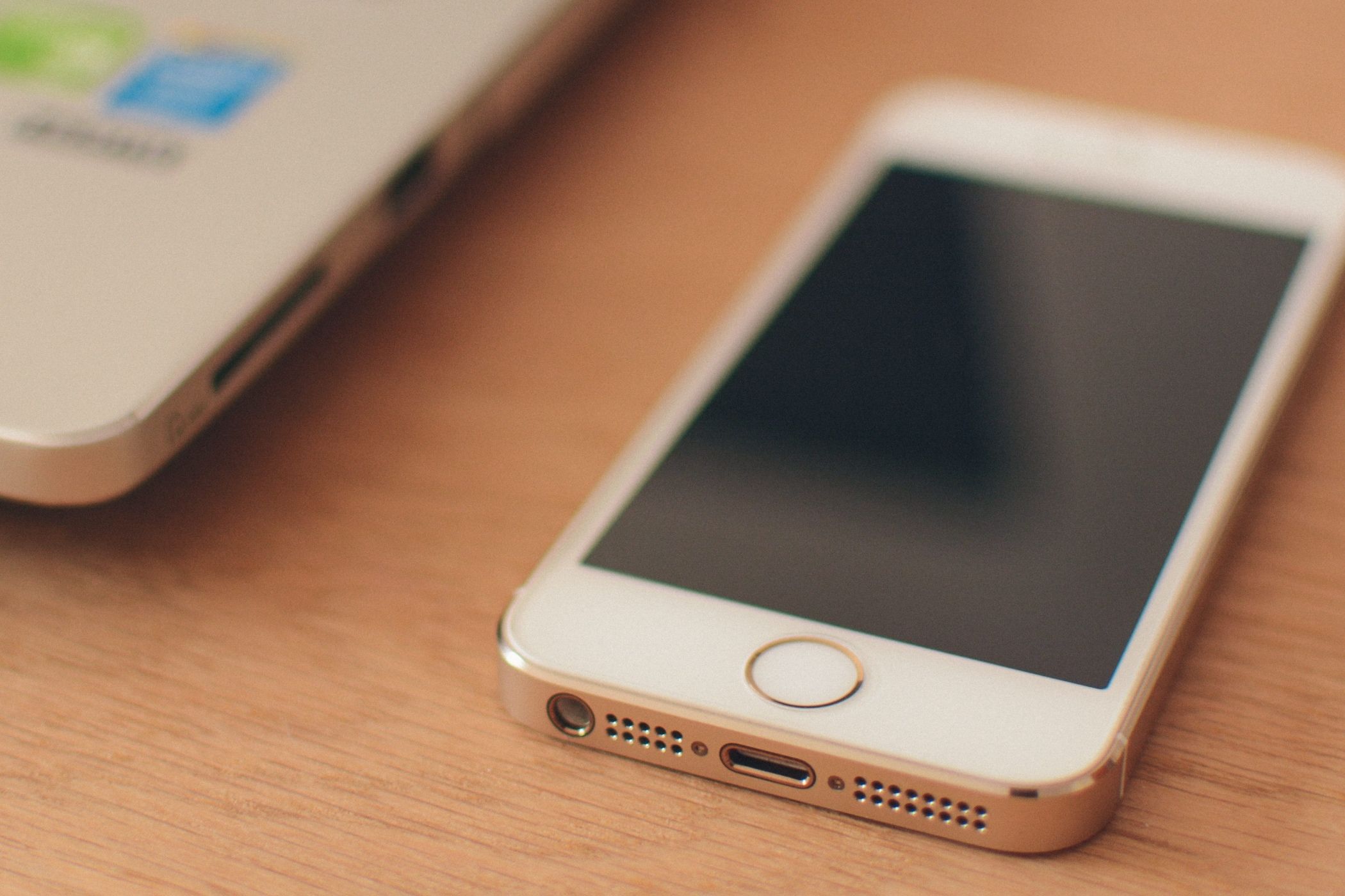 iPhone 5s gold and white variant on a brown desk with a laptop in background