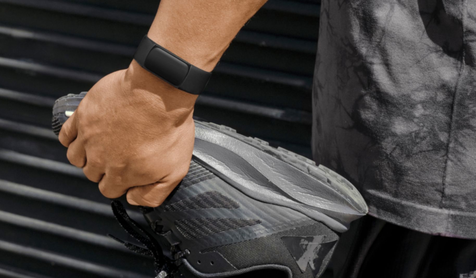 A hand holding a shoe while wearing a Fitbit Charge 6.
