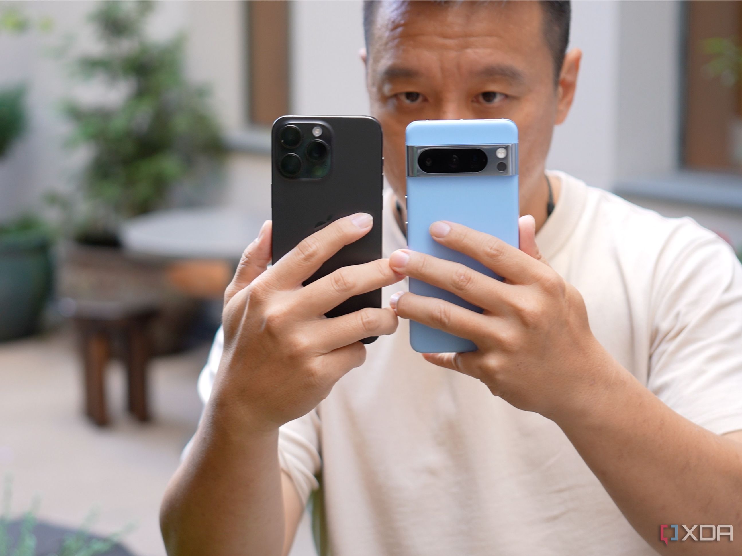 A dude holding the iPhone 15 Pro Max and Google Pixel 8 Pro in his hands