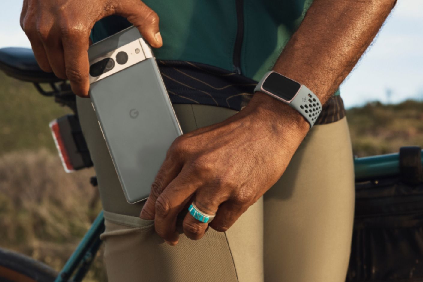 A hand inserting a Pixel phone into a pocket while the other hand wears a Fitbit Charge 6 on the wrist.