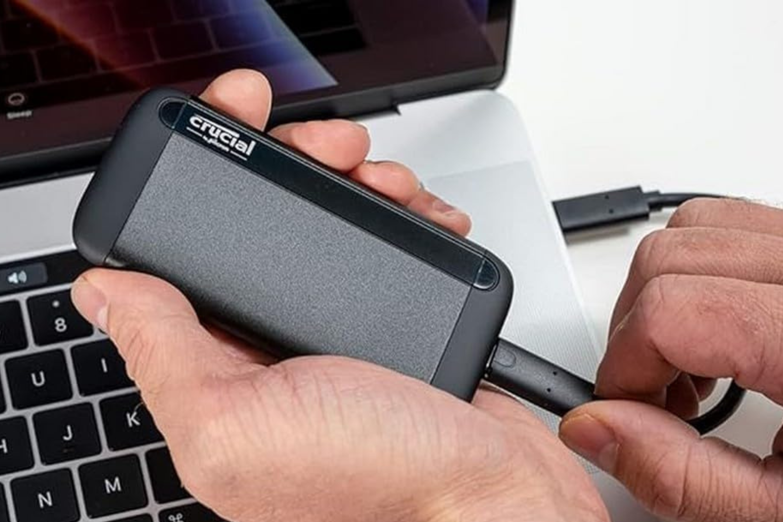 Crucial X8 Portable SSD in hand being plugged into computer 