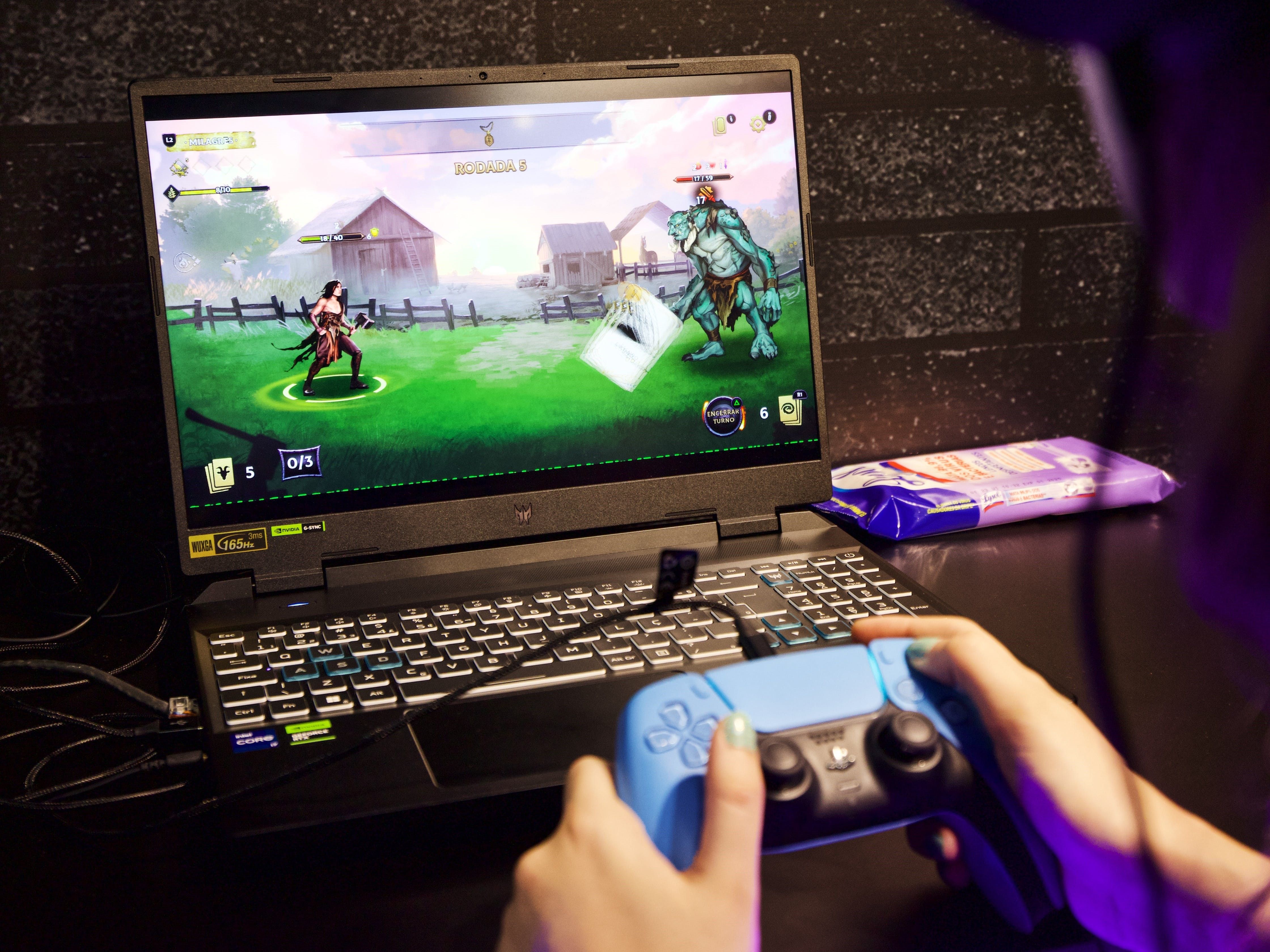 человек, держащий контроллер PlayStation во время игры в видеоигру на портативном компьютере