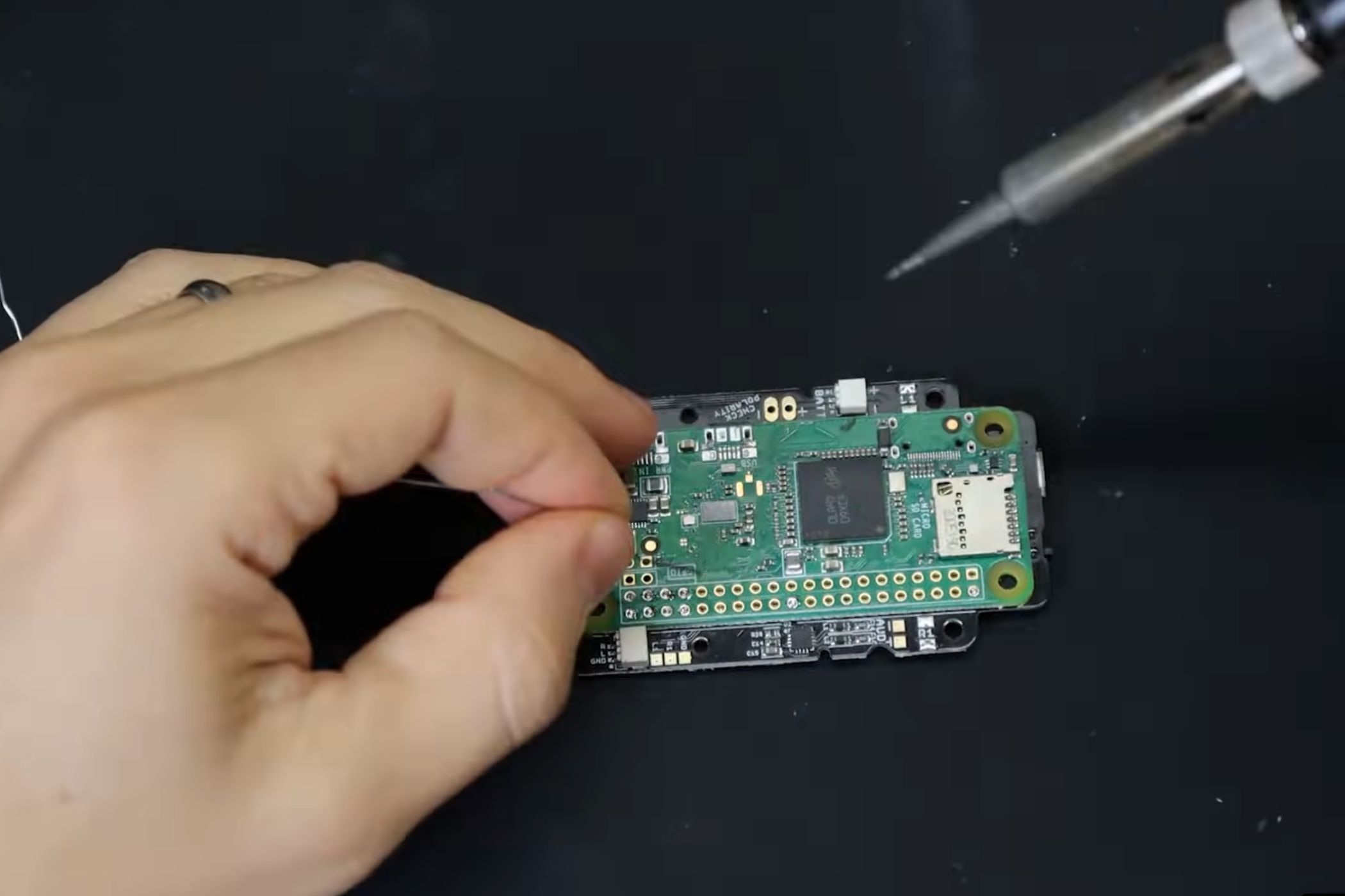 Una captura de pantalla que muestra a una persona soldando un módulo Raspberry Pi a una PCB.