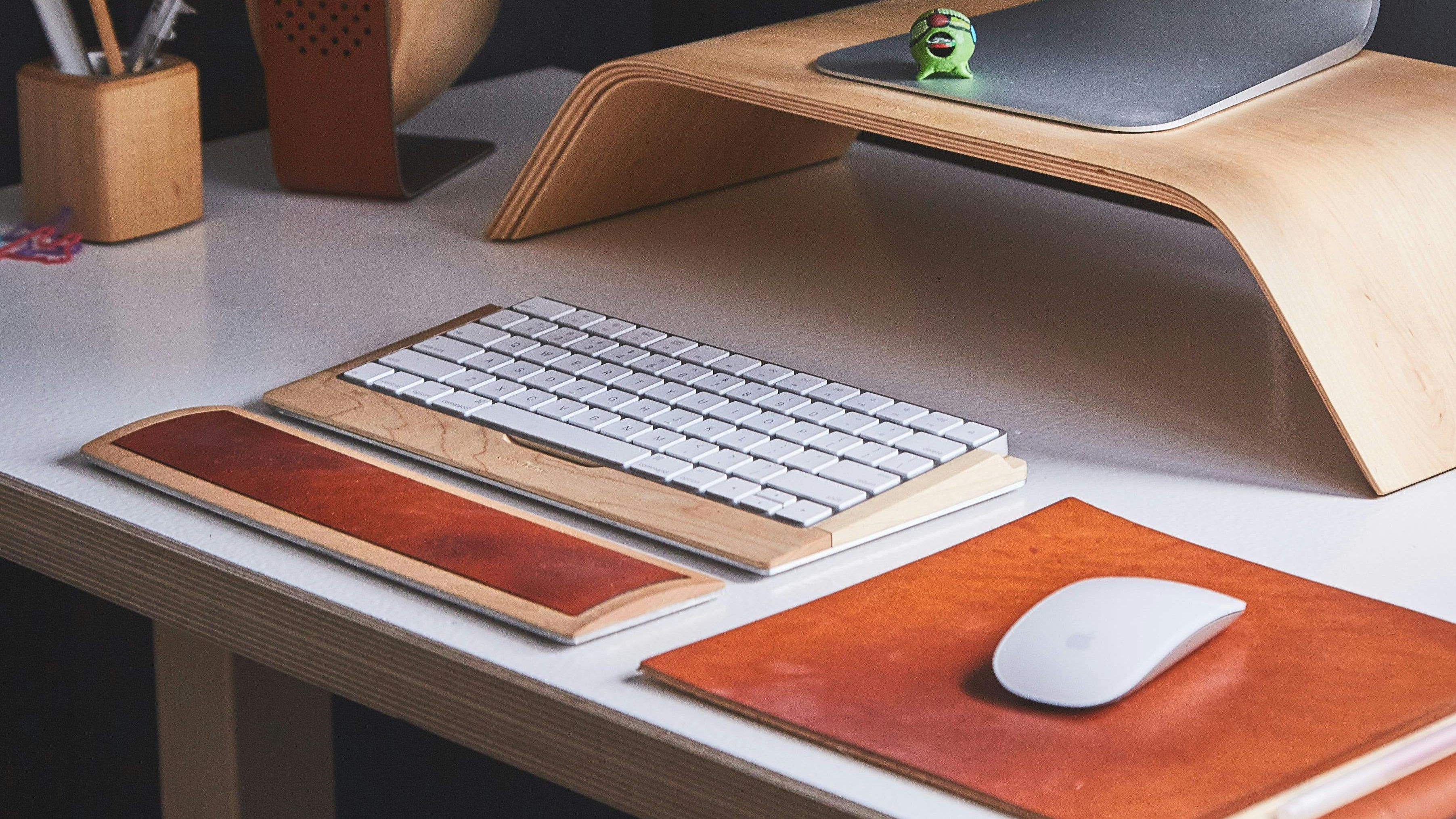 Un teclado de madera junto a un ratón y un reposamuñecas sobre un escritorio blanco.