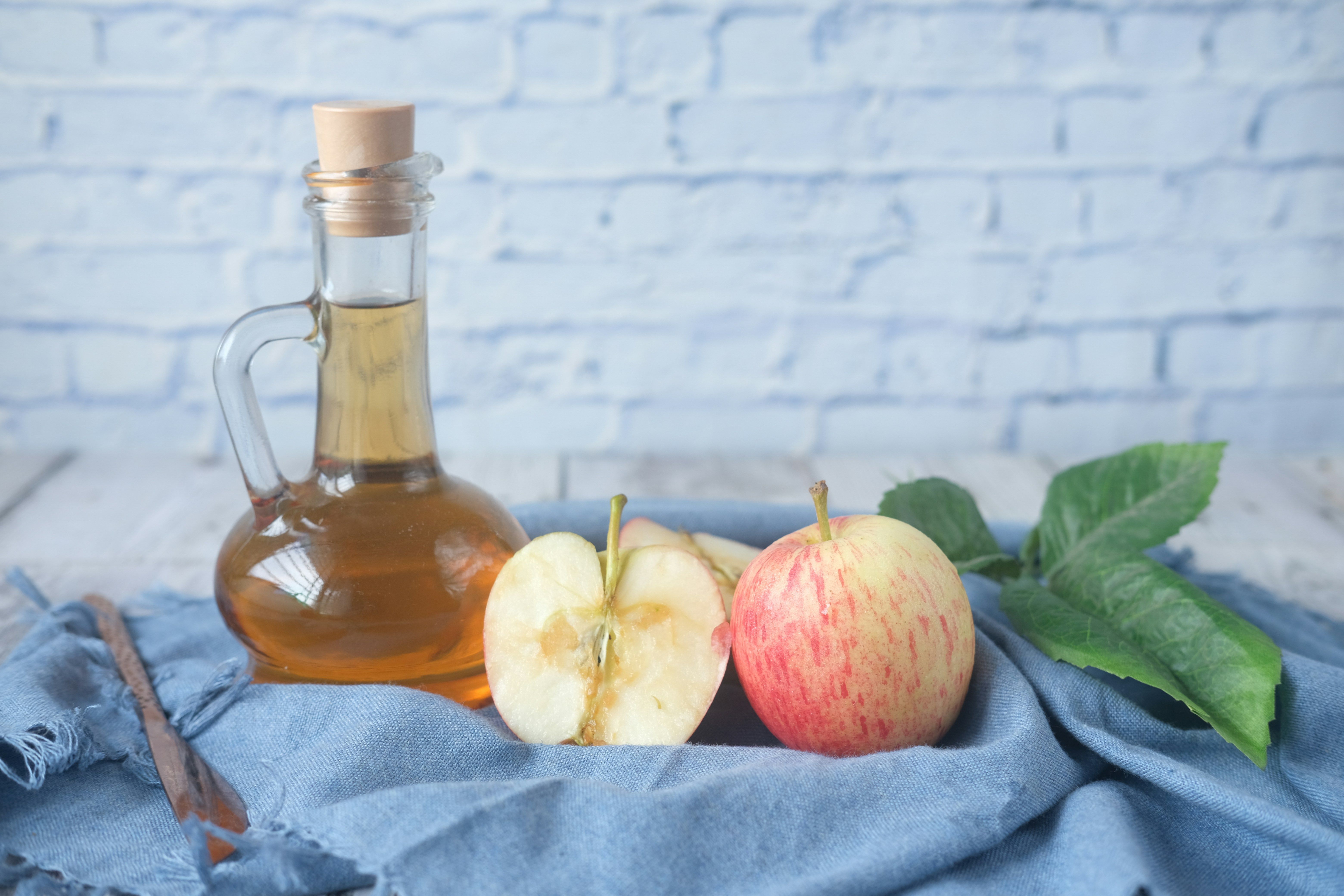 Una botella de vinagre junto a manzanas y hojas de menta.