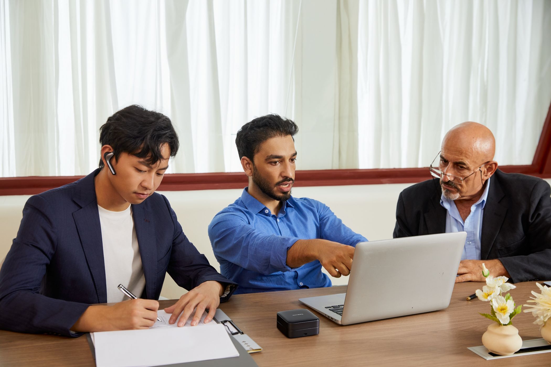 Tres hombres haciendo negocios, uno de ellos con un auricular Timekettle