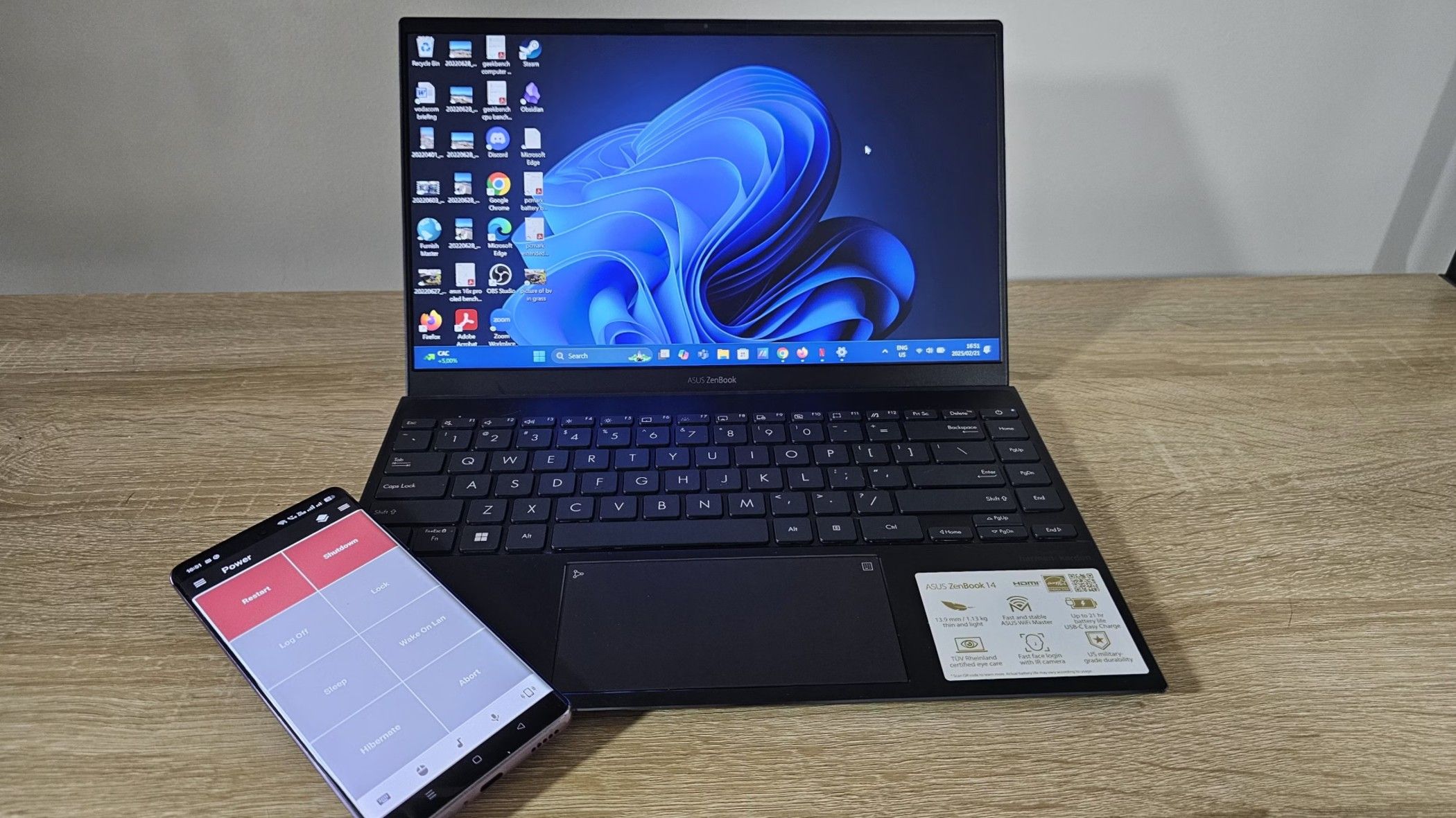 The Asus ZenBook open with Windows 11 screen and an Android smartphone on the side