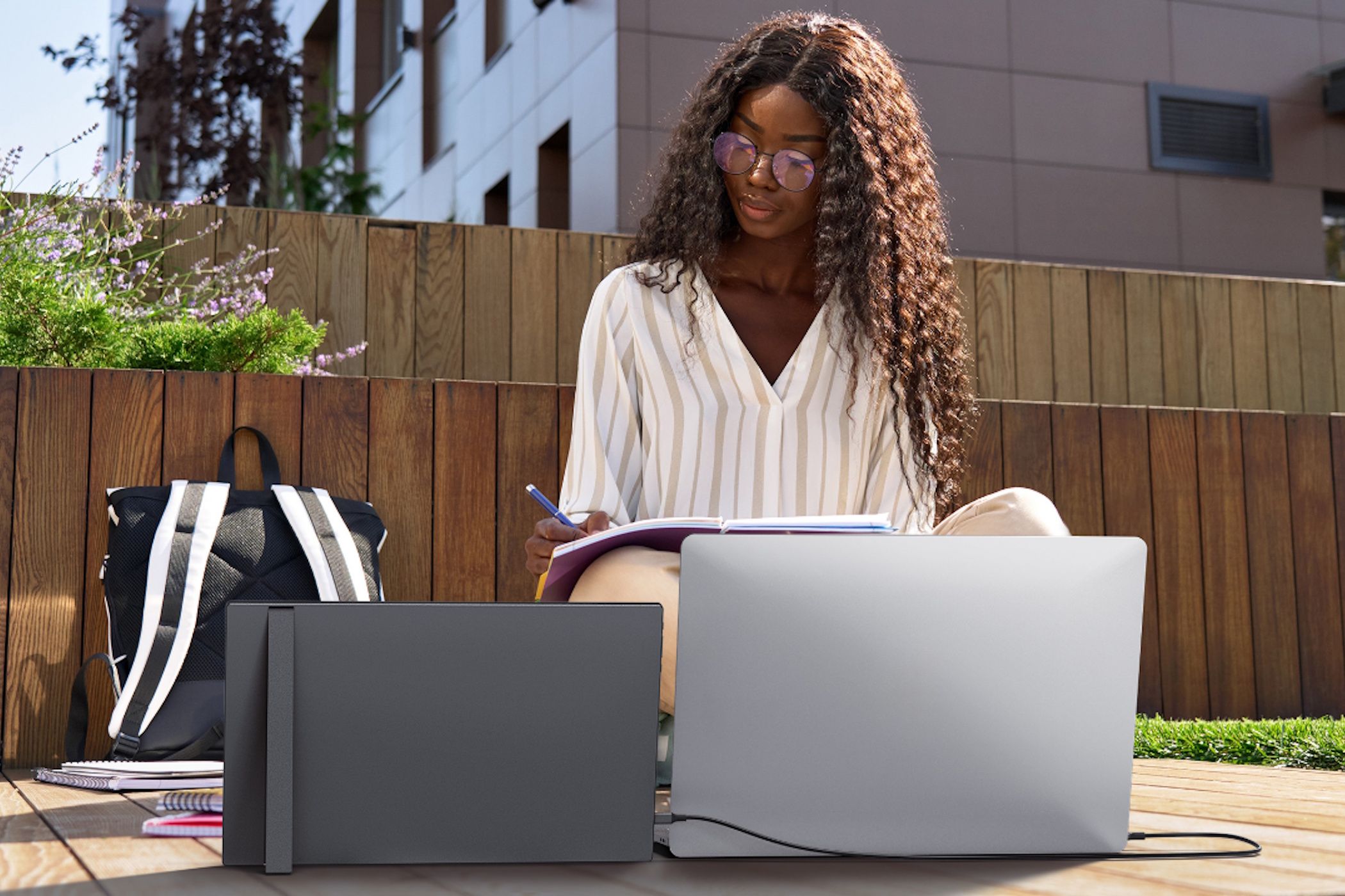 Woman using a laptop and portable monitor outside.