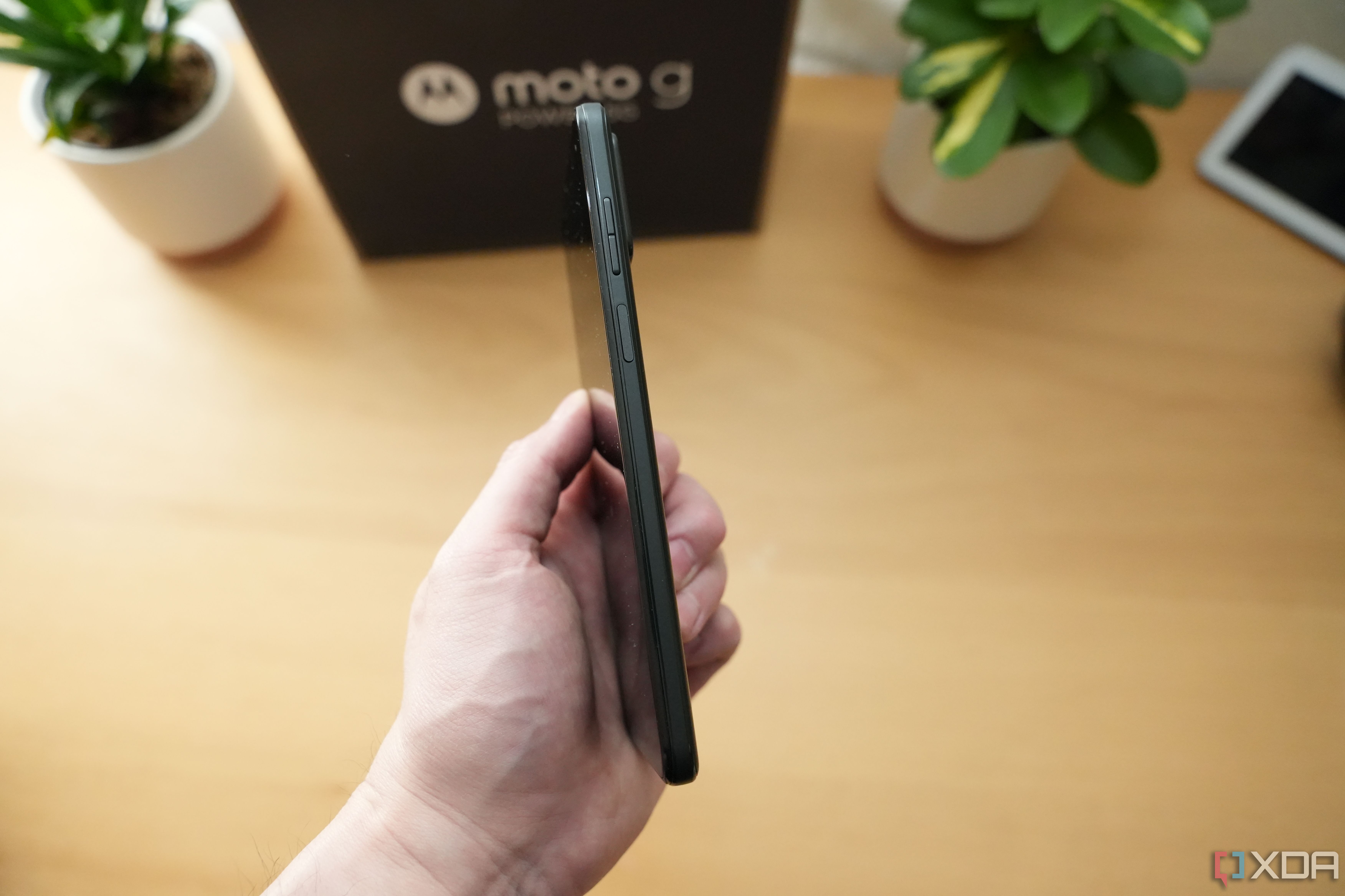 Motorola G Power 5G 2023 side view showing volume rocker and power button in front of wood tablet with plants and Motorola packing in the background