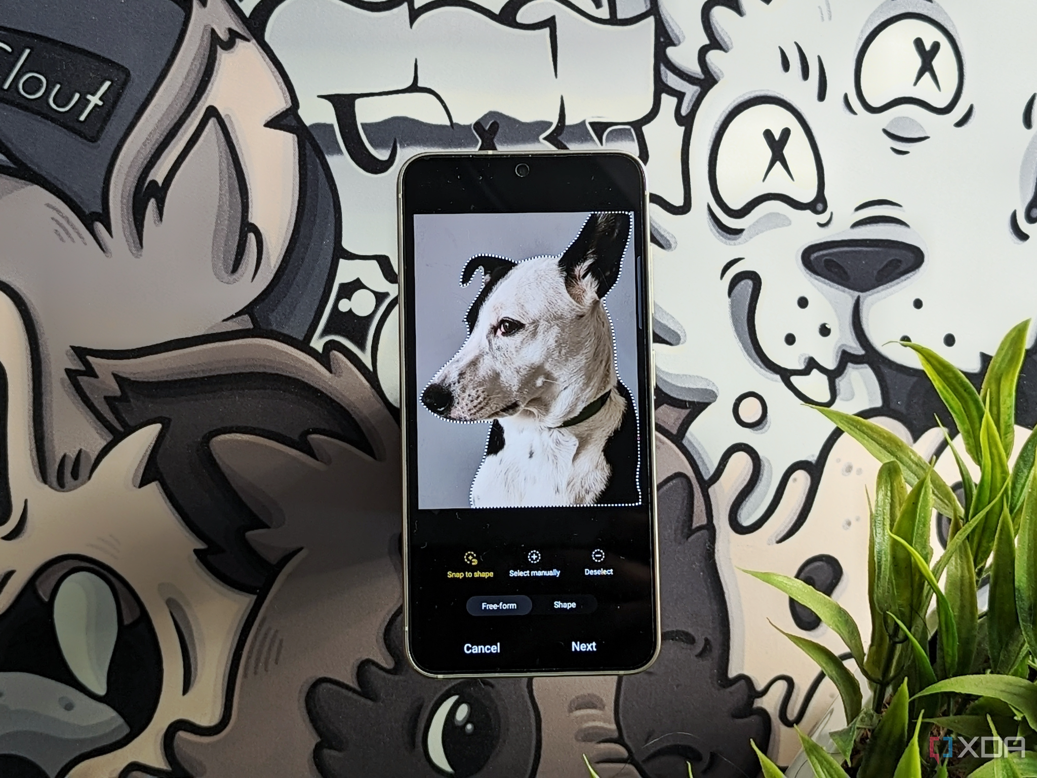 An image showing a picture of a dog on a Galaxy S23 that's kept on a GAF deskmat next to some plants.